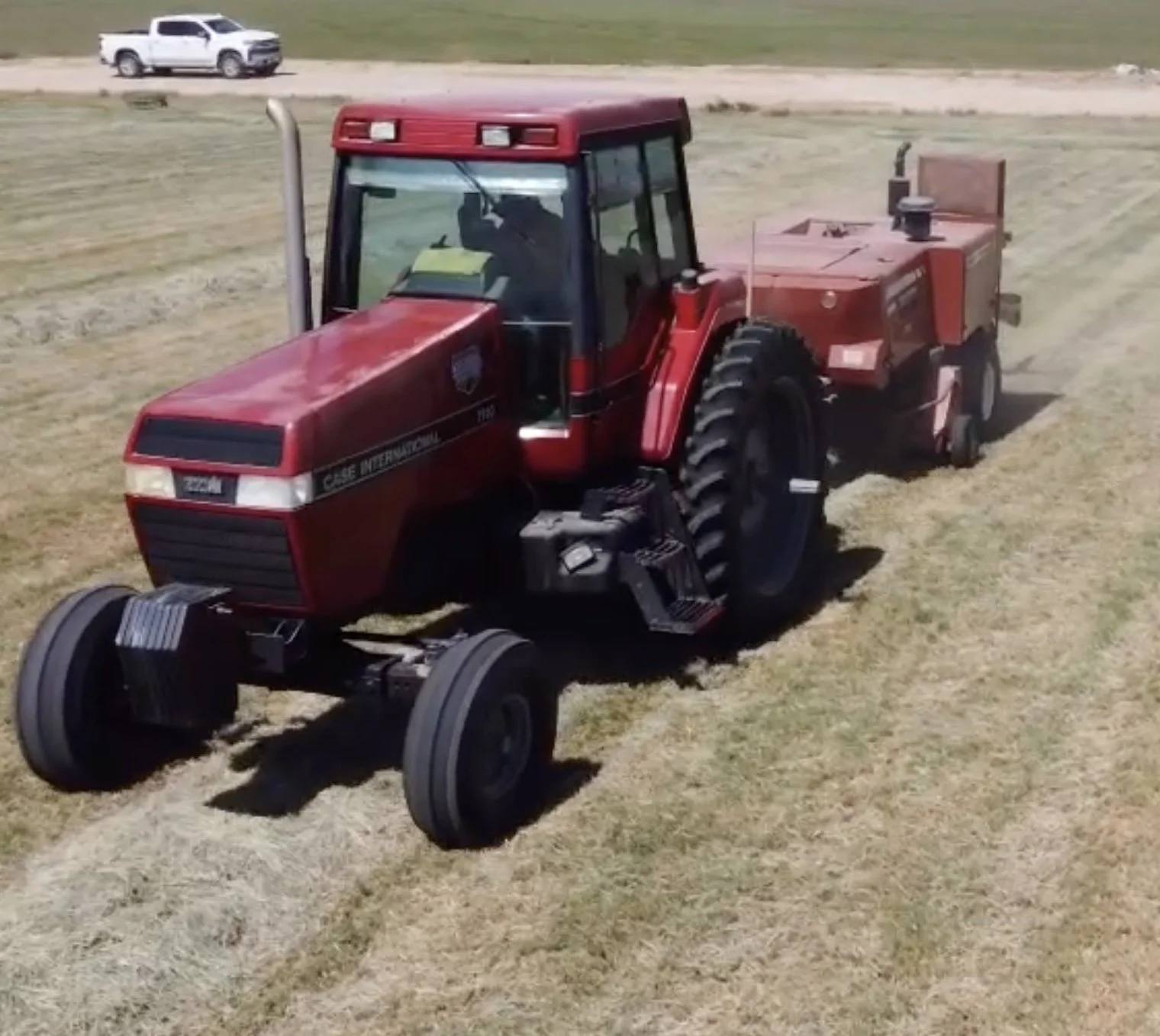 Red tractor with a front cab and large rear wheels, pulling a farming implement across a field.