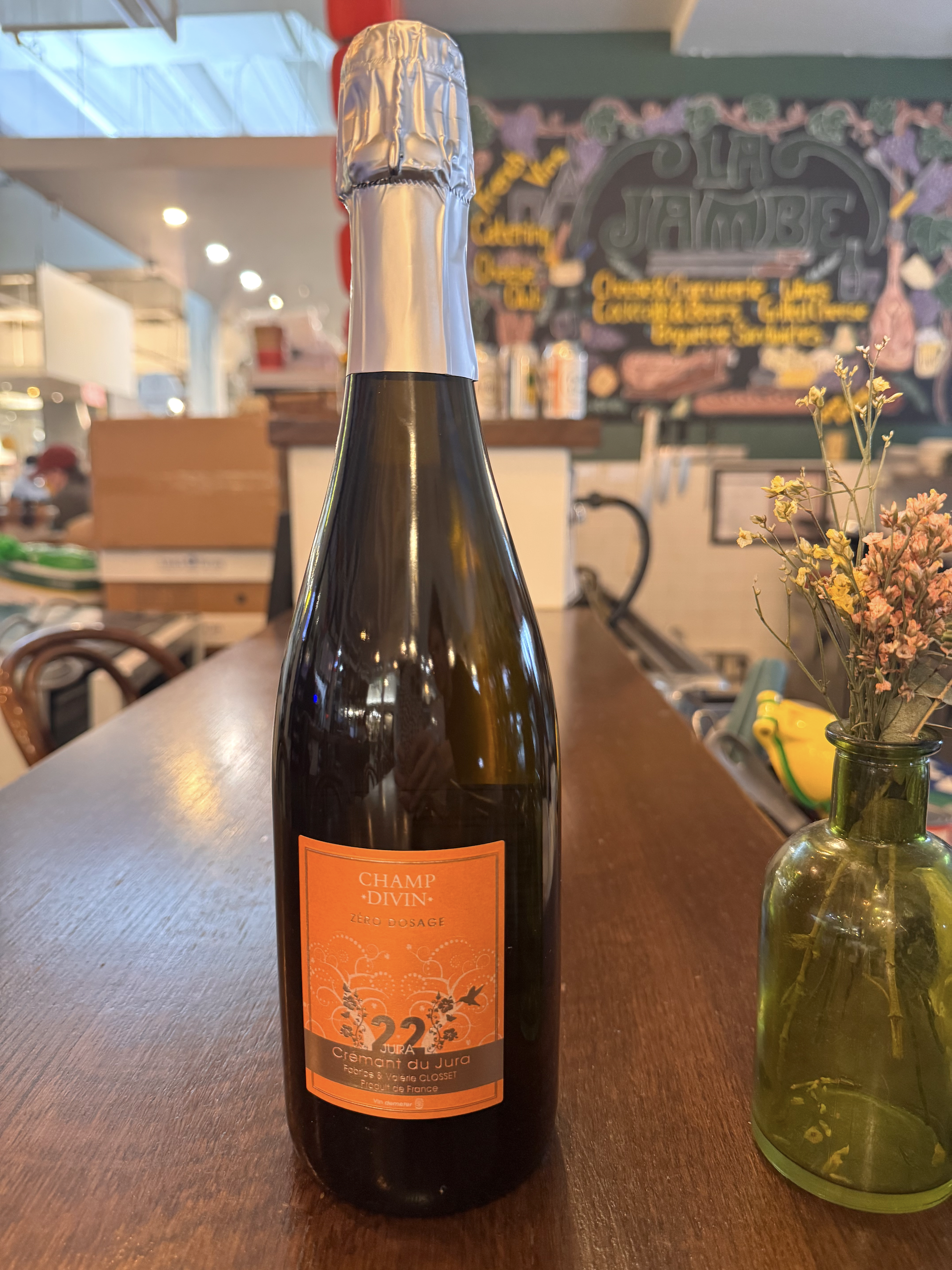 A dark glass bottle of sparkling wine with a white foil cap, placed on a wooden surface with 