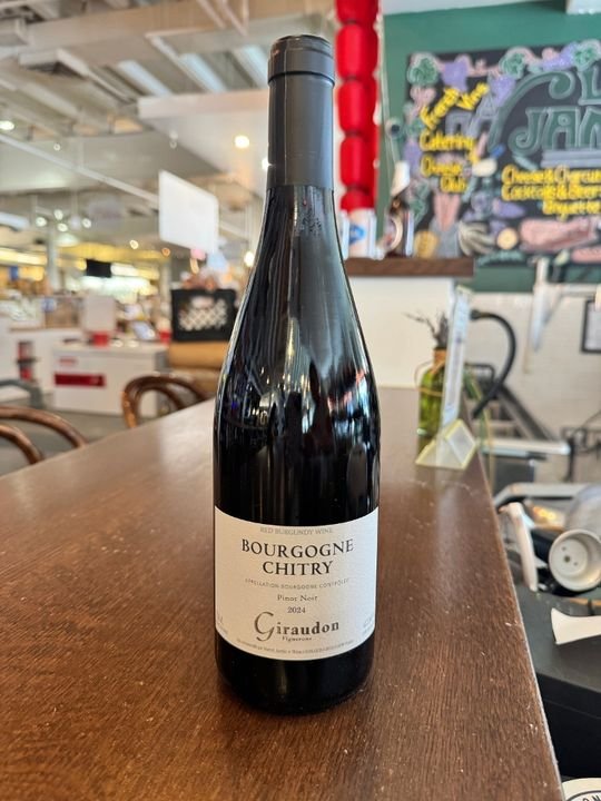 A bottle of Bourgogne Chitry Pinot Noir wine on a wooden table in a restaurant or cafe setting.