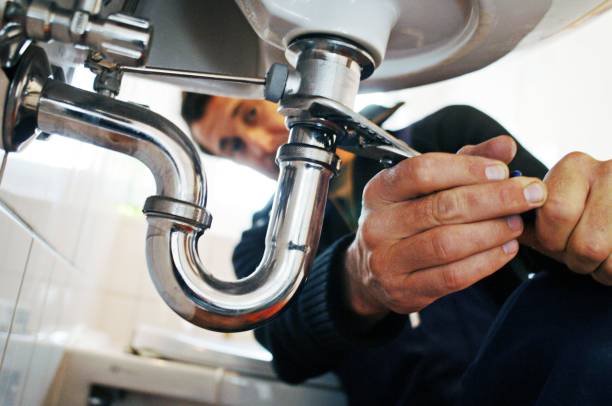 A person repairing or inspecting a kitchen sink plumbing under the sink.