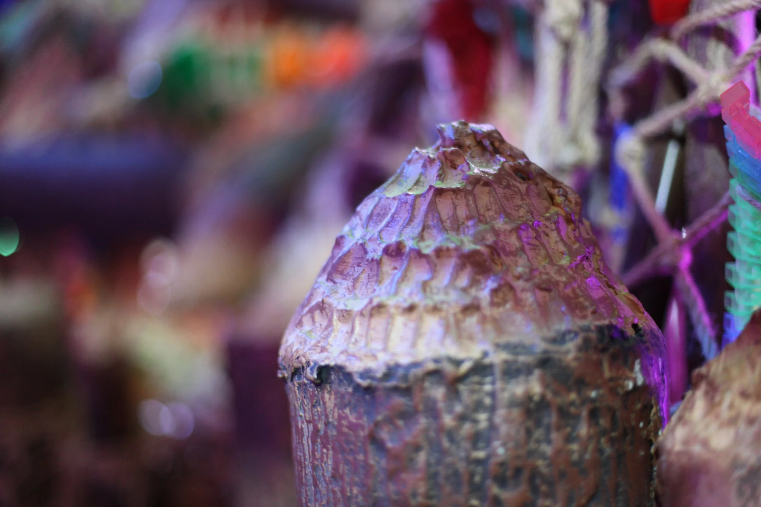 Close-up of a brightly colored, textured sculpture at Atlas9 with a cone shape, surrounded by blurred colorful objects.