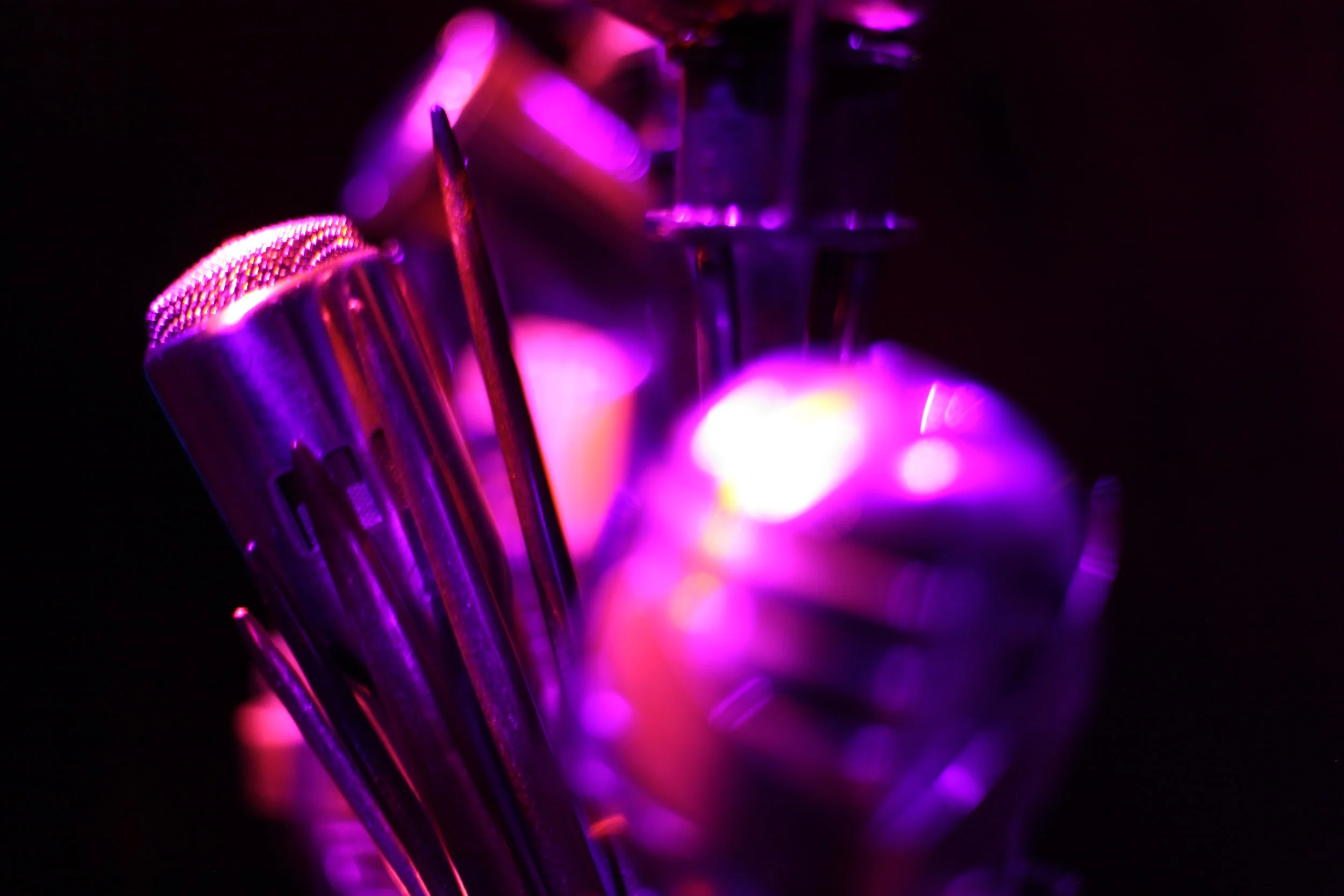 Close-up of metallic objects and tools illuminated with vibrant purple and pink lighting, including a microphone, a file, and various metal parts, against a dark background in the Jazz club of Atlas9