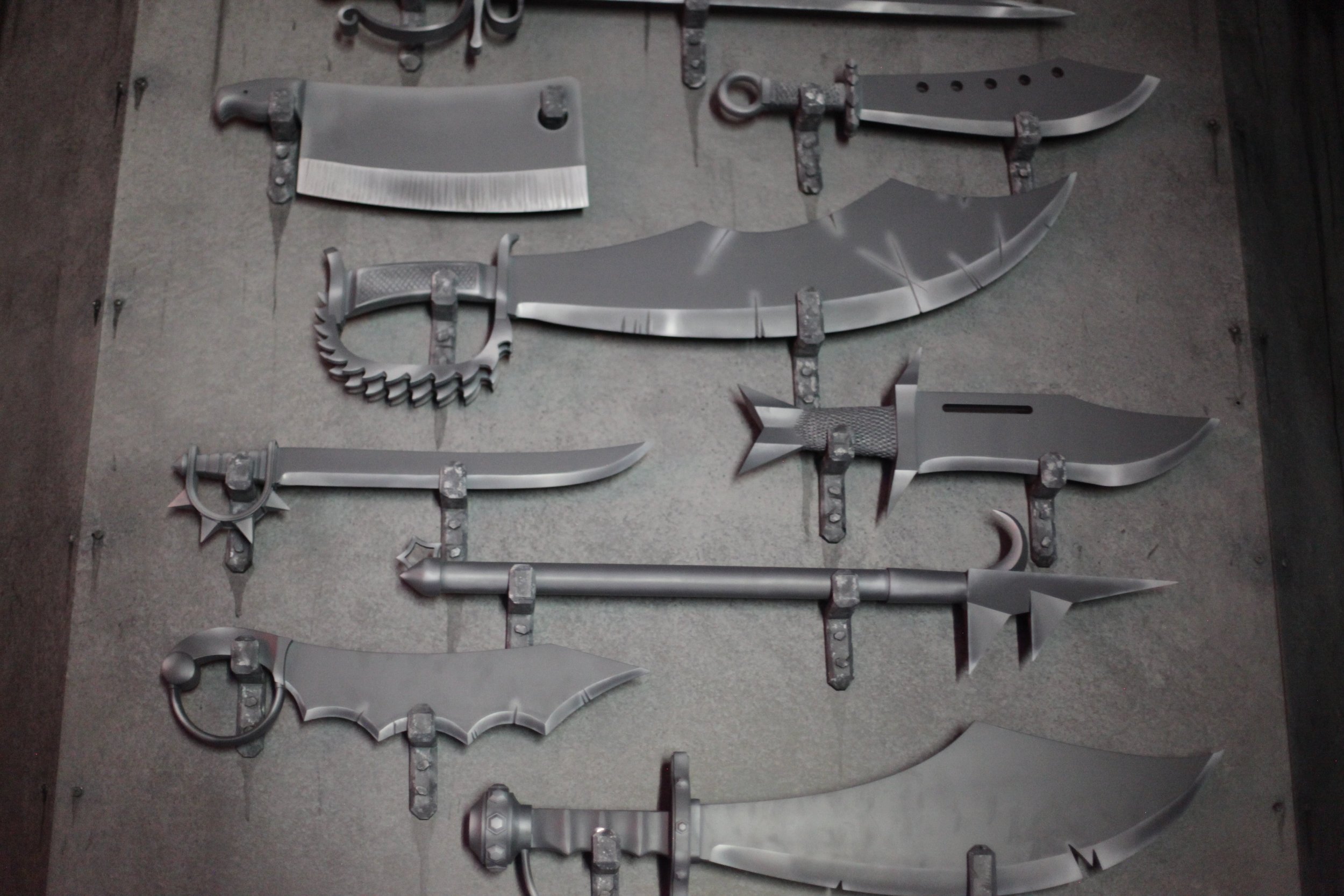 Collection of custom-designed fantasy and medieval-style weapons inside of Atlas9 laid out on a metal surface, including various swords, knives, and blades.