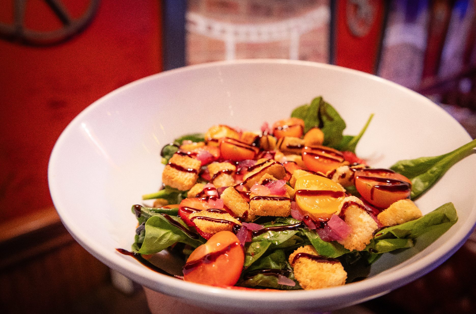 A fresh salad in a white bowl with mixed greens, cherry tomatoes, croutons, red onions, and balsamic glaze drizzle from Splice Bros. Pizza in Atlas9