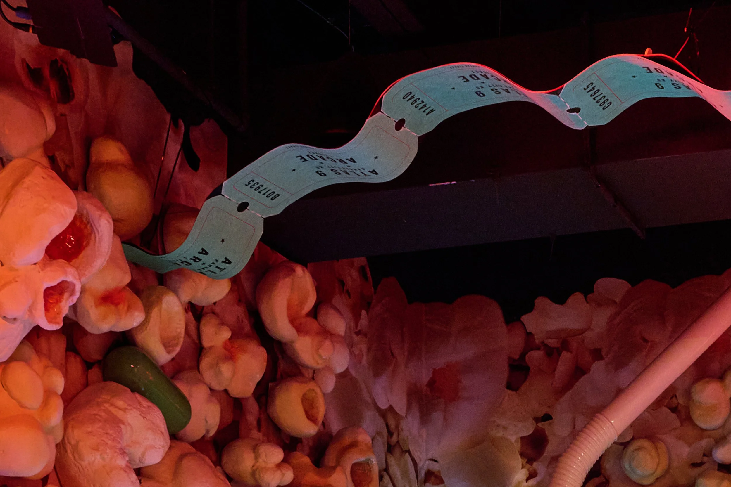 A long strip of movie tickets draped against a black backdrop, surrounded by scattered popcorn and a pickle at Atlas9.