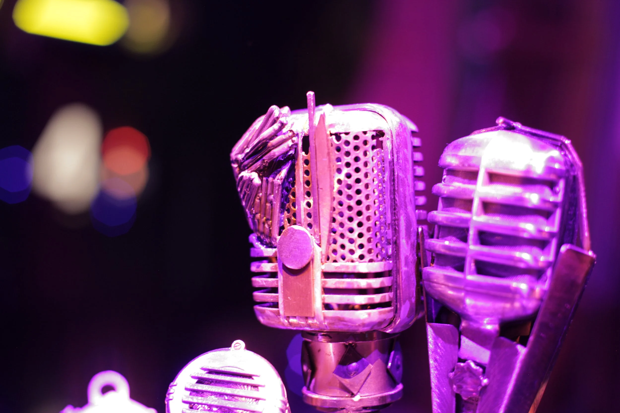 Close-up of several vintage microphones illuminated with purple and pink lighting against a dark background. Jazz club of Atlas9