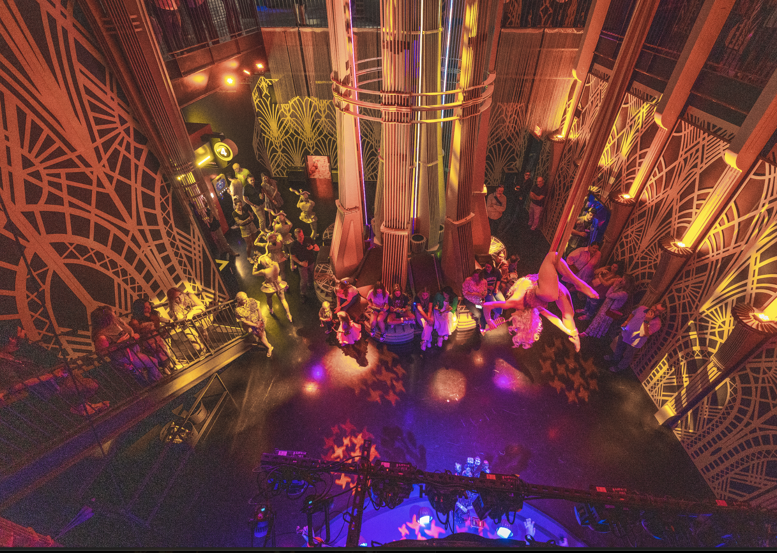 An aerial view of the jazz club at Atlas9 with colorful lights, a center stage with a performer upside down, and people dancing and sitting around the space.