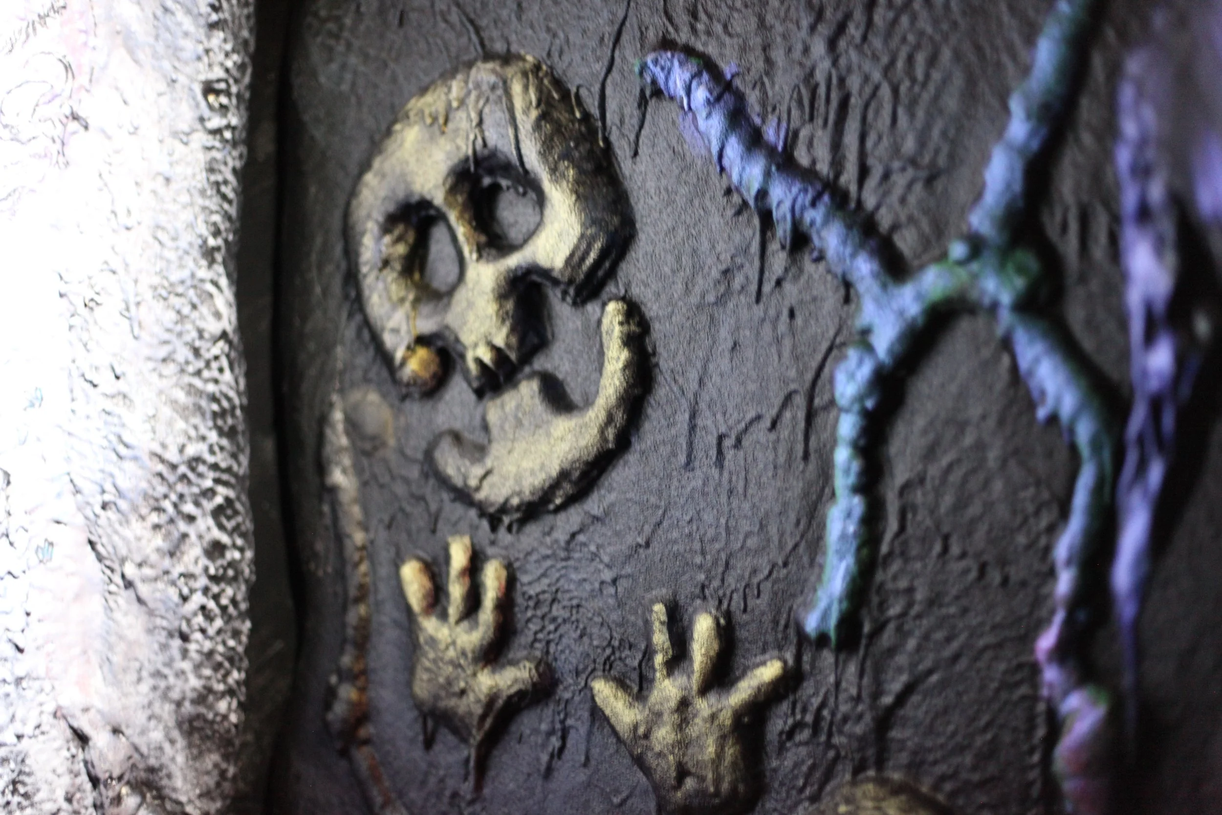 A cartoon textured wall with a carved skull and two handprints, along with a metallic-looking branch or vine inside Atlas9.