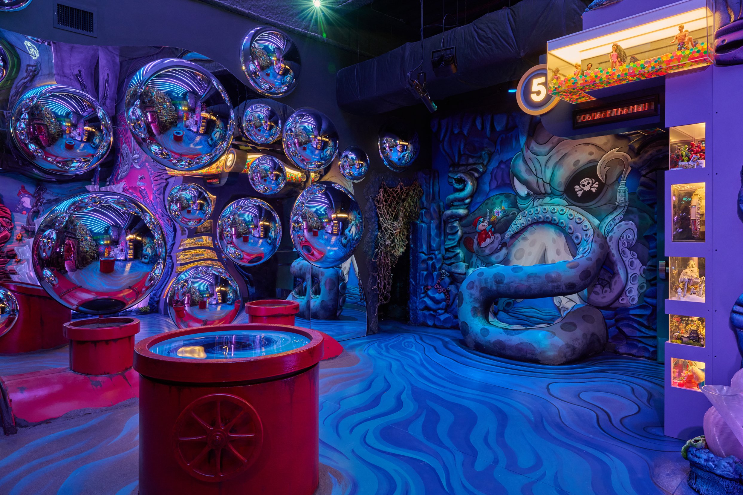 Colorful immersive art room with shiny reflective spheres on the wall, a mural of an octopus, and a claw machine filled with toys.