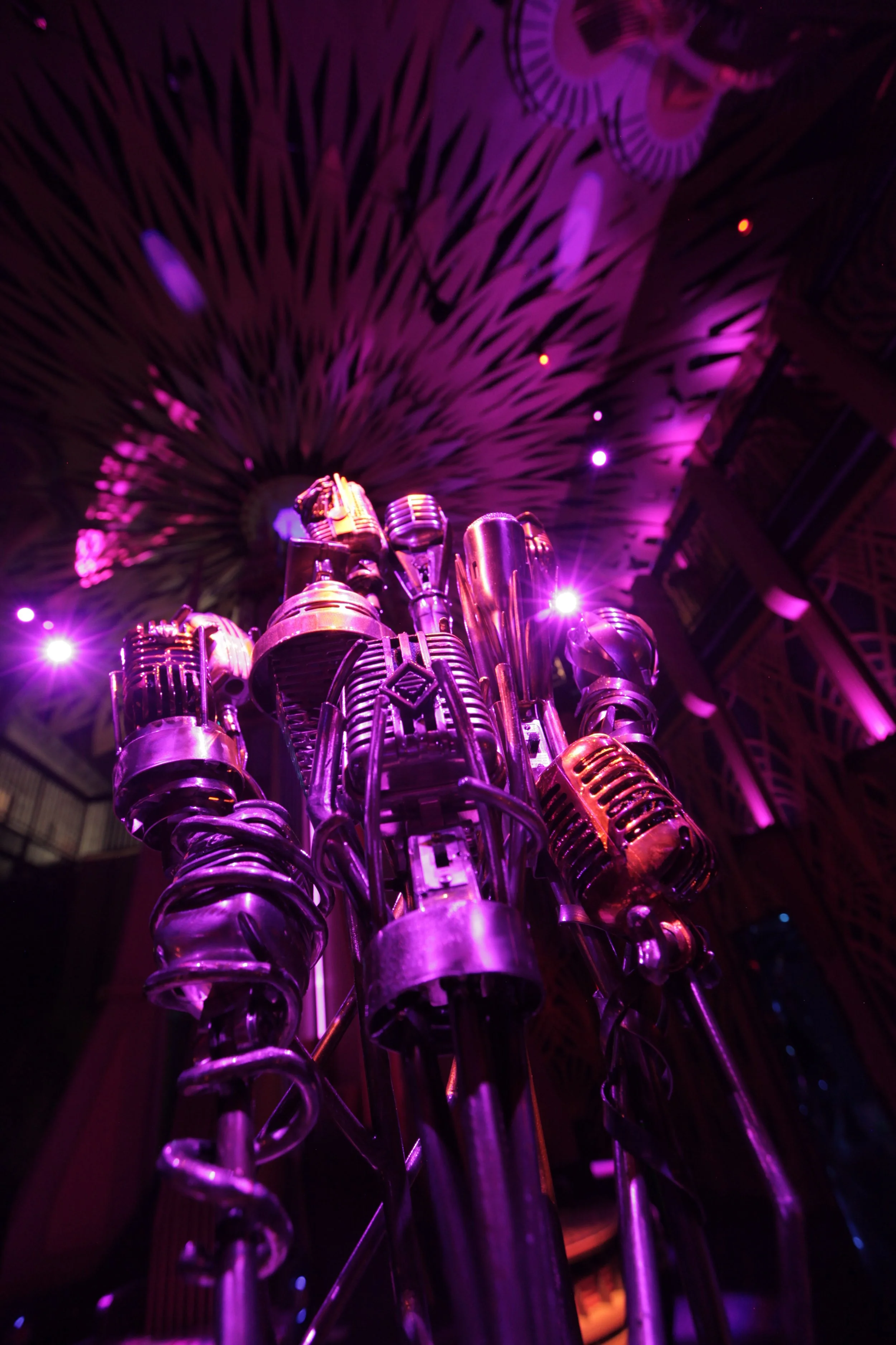 Close-up of shiny brass musical instruments, like trumpets and trombones, illuminated by purple stage lights, with a colorful ceiling in the background in the jazz club of Atlas9.