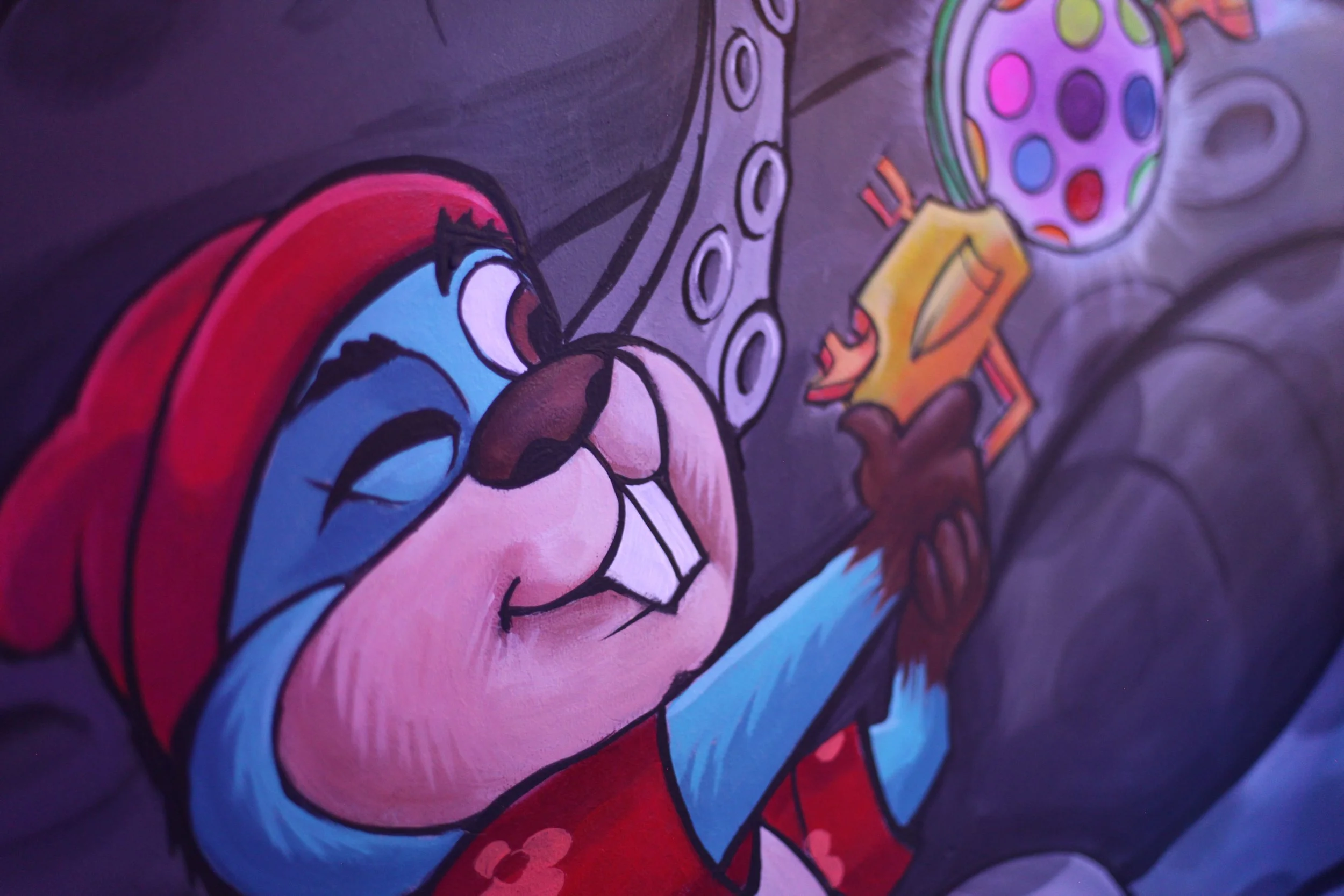 A colorful cartoon mural depicting a character with blue skin, red hair, and glasses, holding a paintbrush and painting a circular object with multi-colored dots.