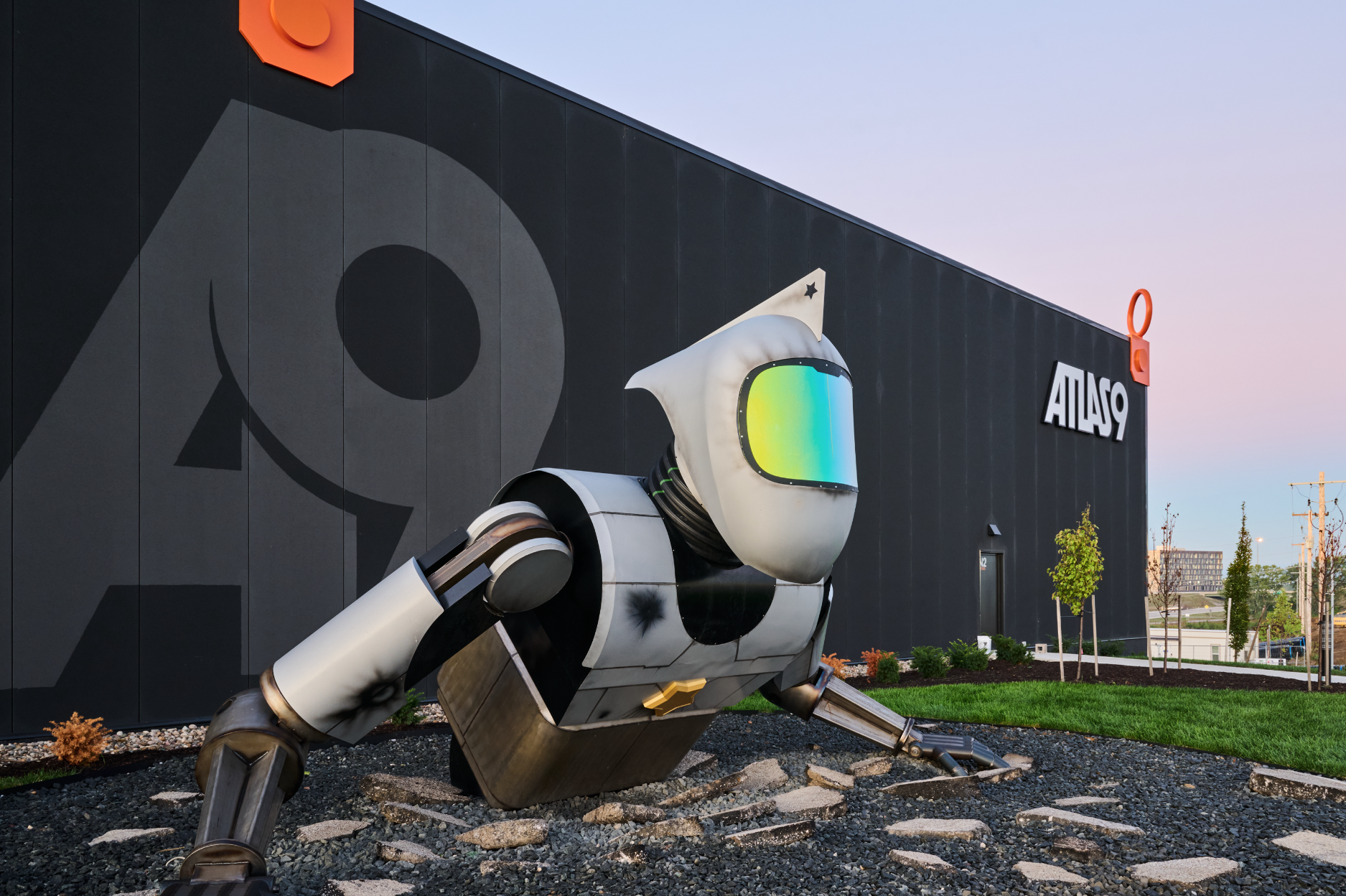 Large robot sculpture at Atlas9 crouching with one arm on the ground, in front of a dark building with the word 'A9' on it.