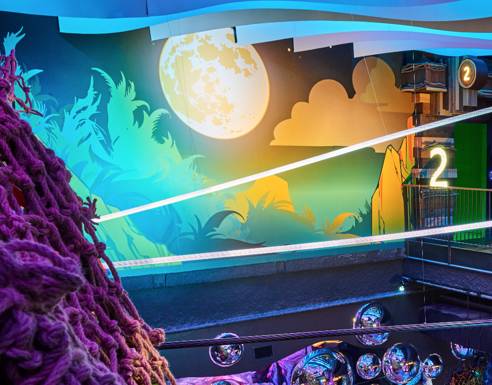 Colorful mural of a full moon, clouds, and silhouette of trees on a wall, with neon lighting and decorations in the foreground.