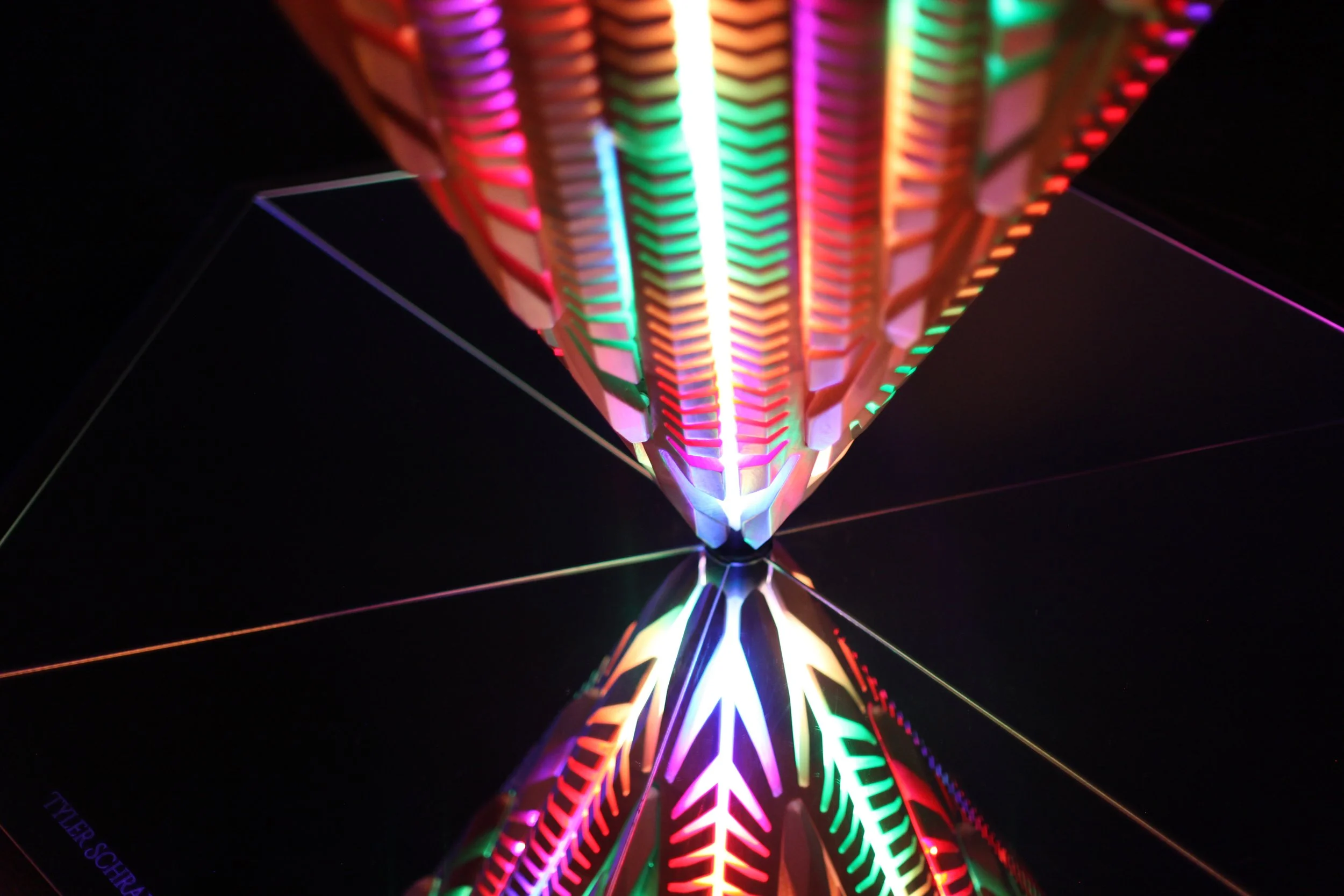 Colorful, illuminated geometric art piece with intricate patterns, reflecting on a mirrored surface.