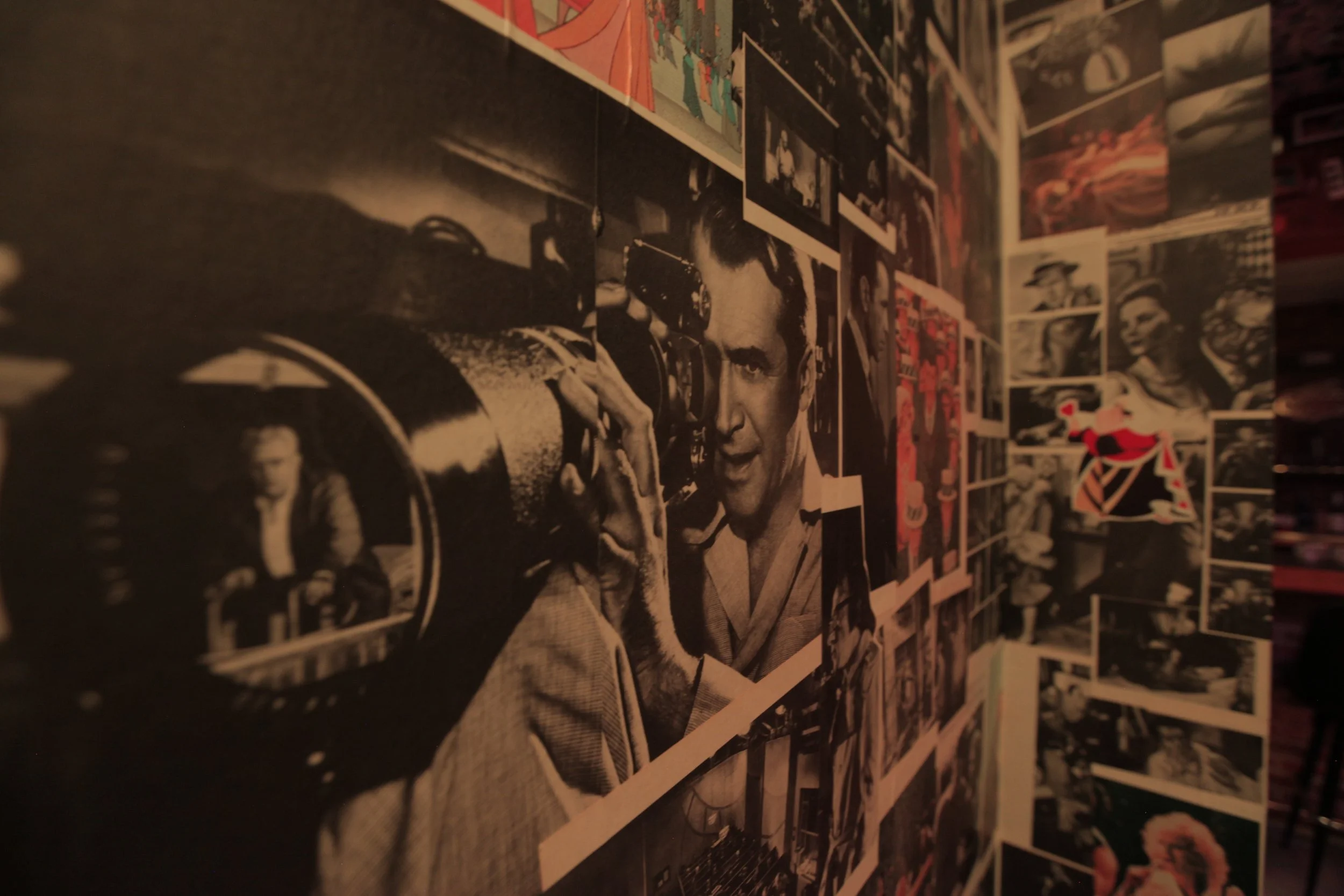 A black-and-white collage of vintage photographs and movie scenes, including a prominent image of a man with styled hair holding a camera. The collage decorates a corner wall.