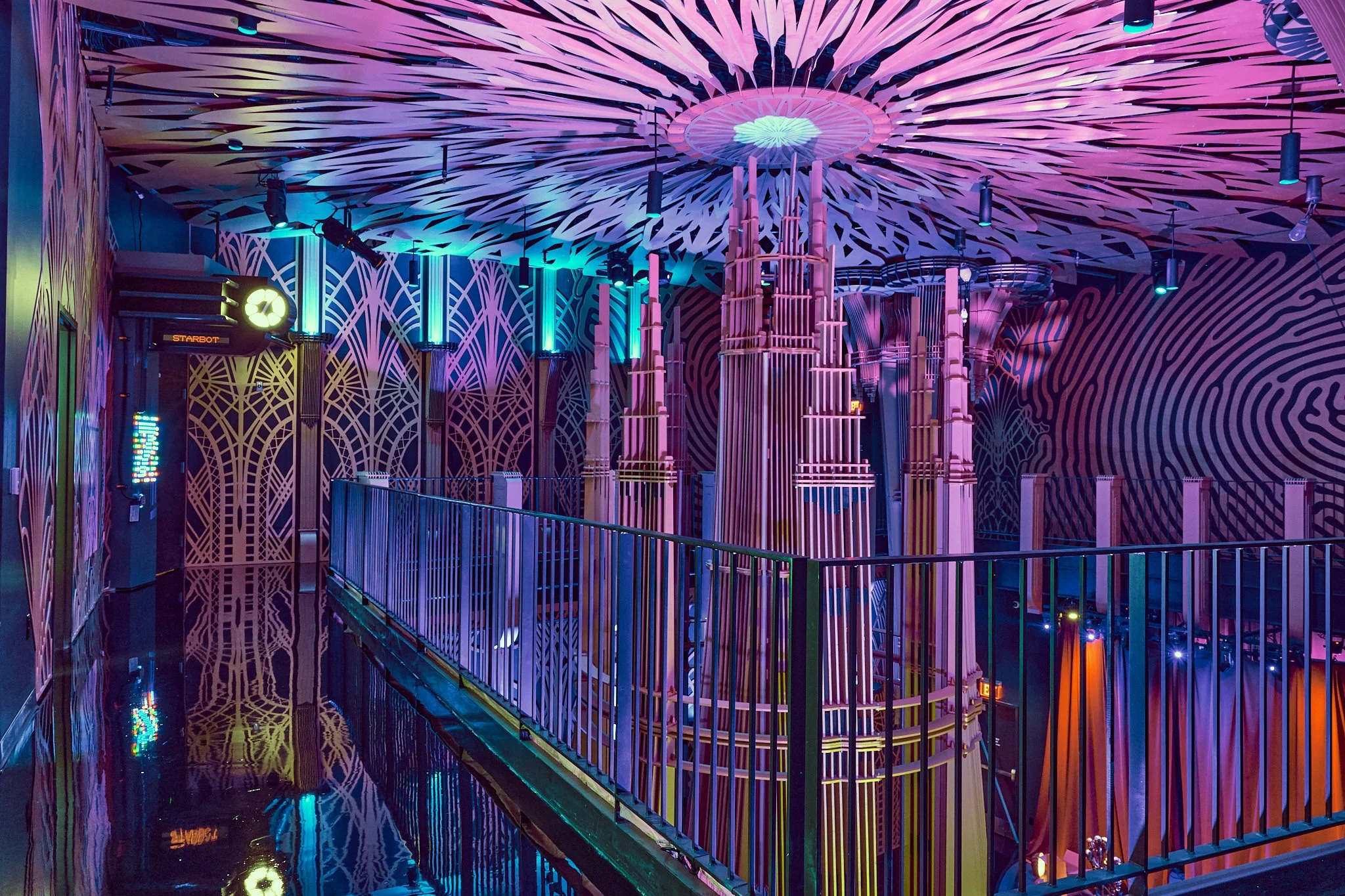 Colorful indoor amusement park with neon lights, decorative patterns on walls and ceiling, and a walkway with a railing.