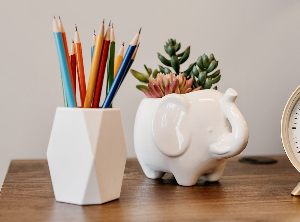 Closeup detail of Dr. Christine Howard's office, including a white cup holding colorful pencils, a white elephant-shaped planter with succulents, and part of a clock on a wooden surface.