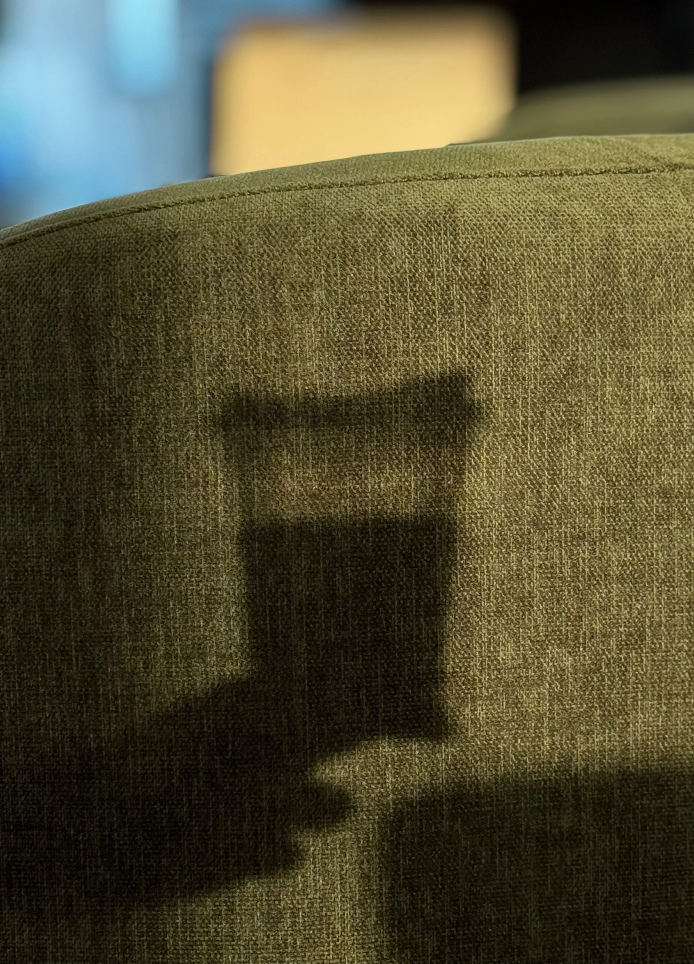 Close-up of a textured green fabric surface with a shadow of a person holding a phone, capturing the photograph.