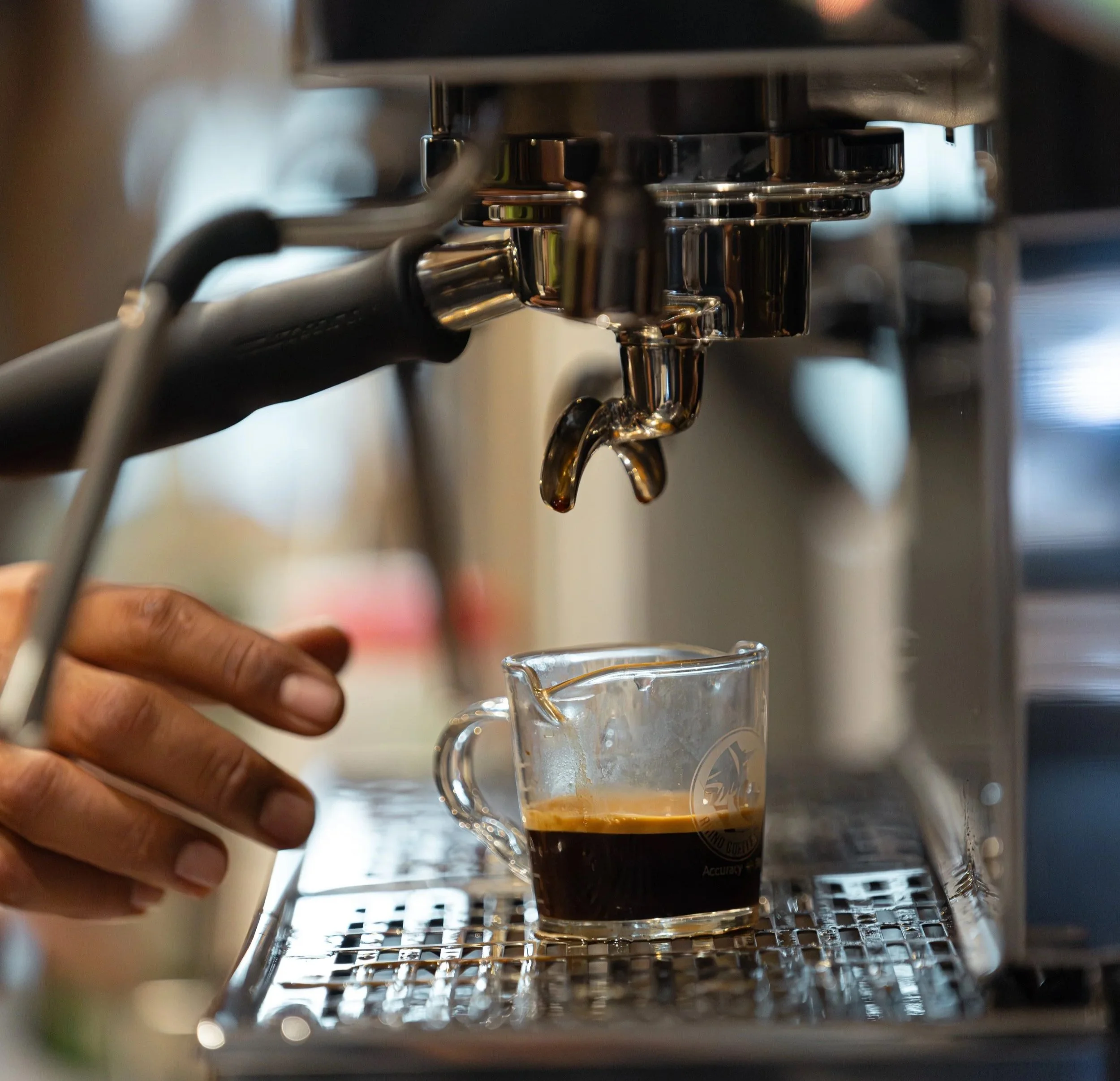 Close-up of an espresso machine pouring coffee into a glass cup with a handle.