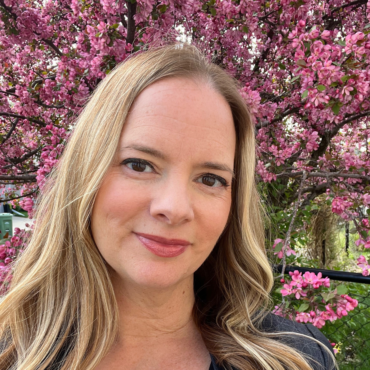 Woman with long hair standing in front of a cherry blossom tree in bloom