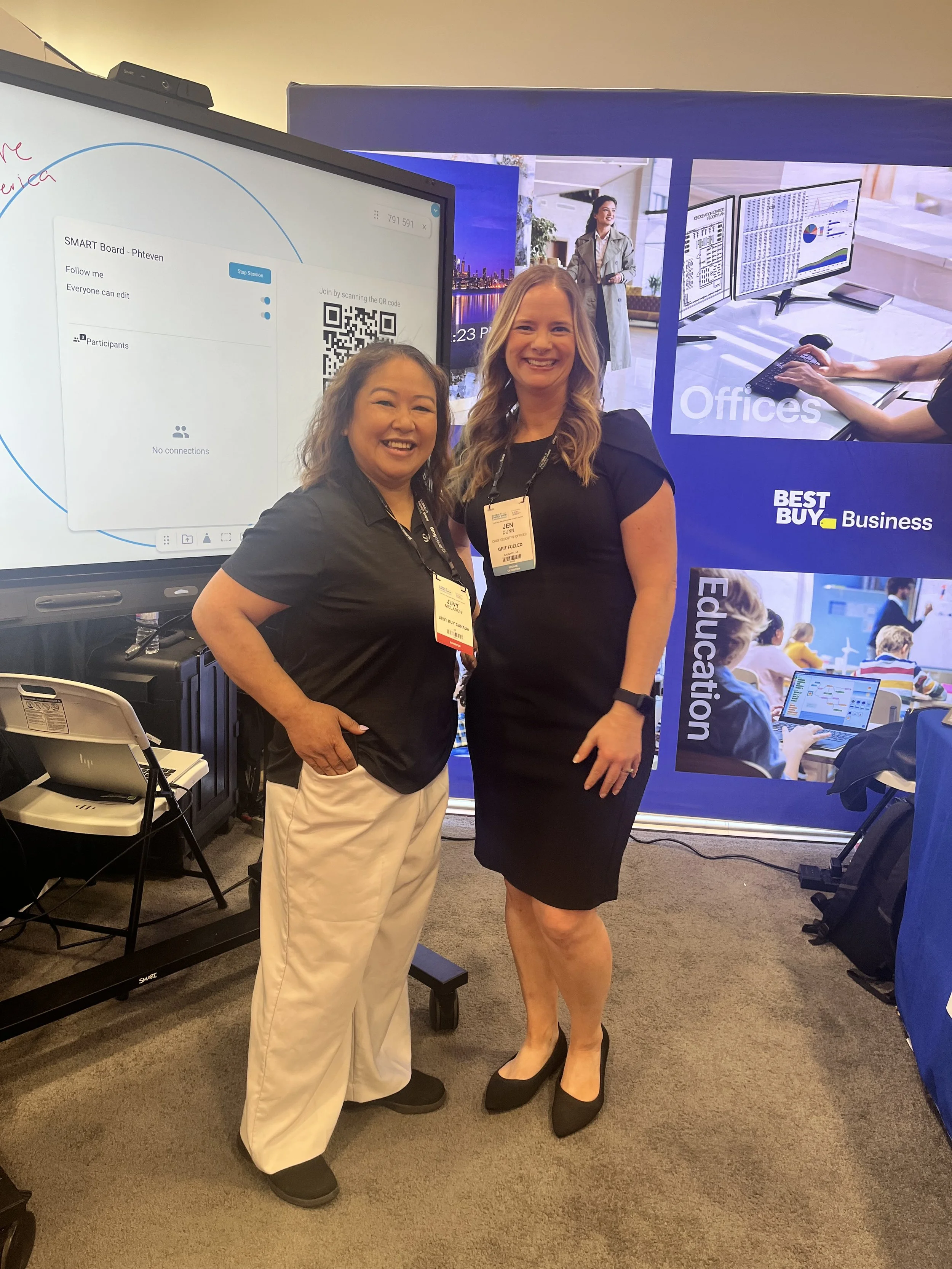 Two ladies smiling, posing for a picture  in a tradeshow booth