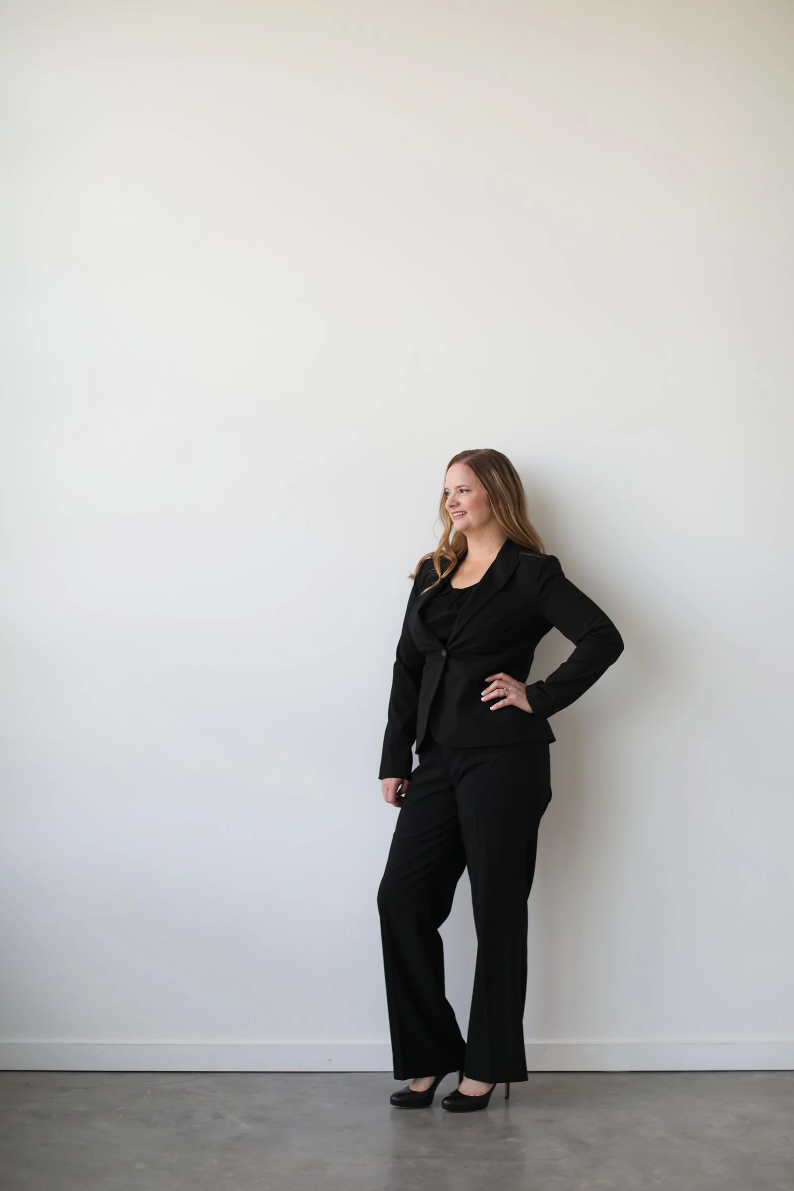 Grit Fueled's CEO , wearing a black suit and high heels, standing against a wall.