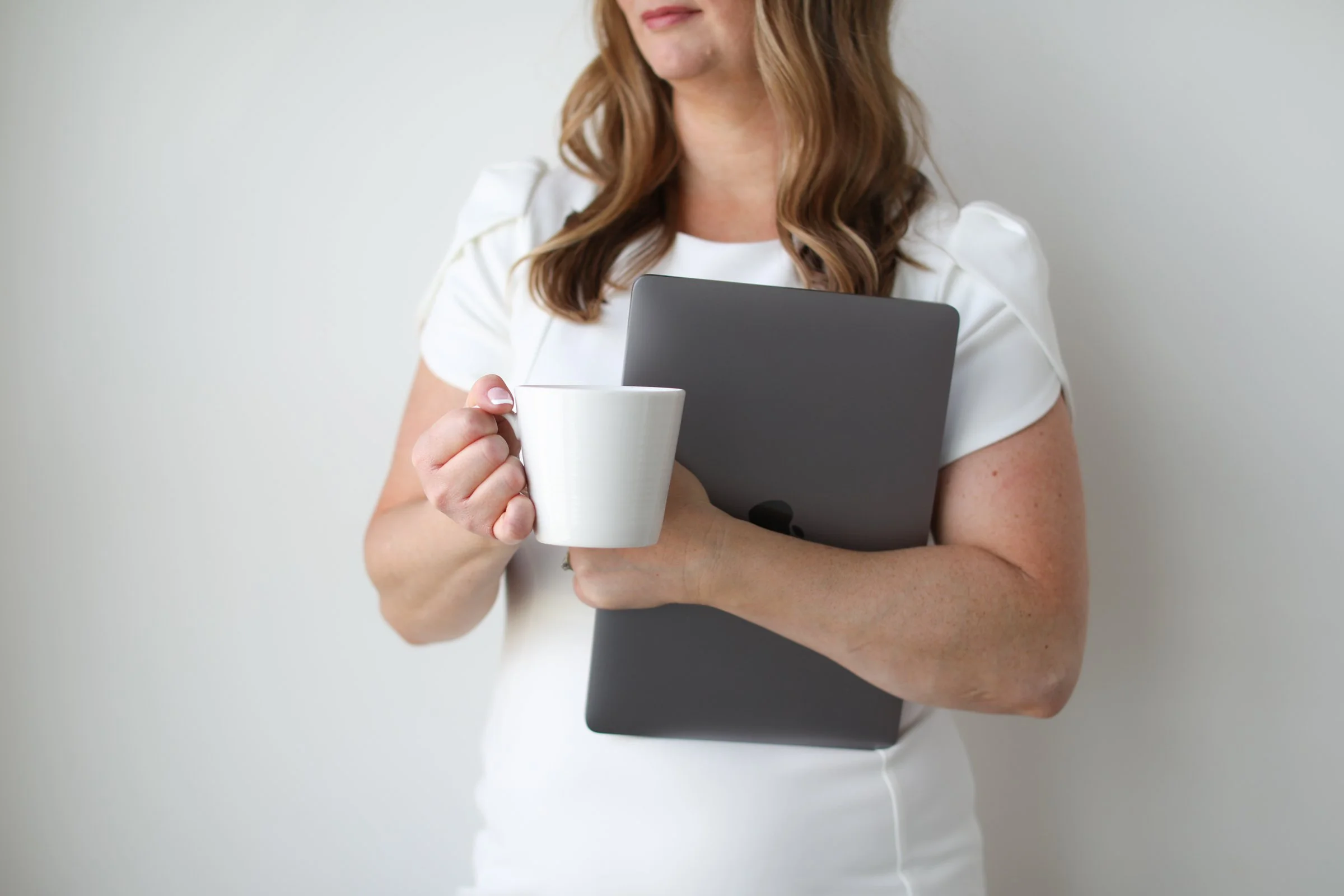 Female business owner holding a closed laptop and coffee cup