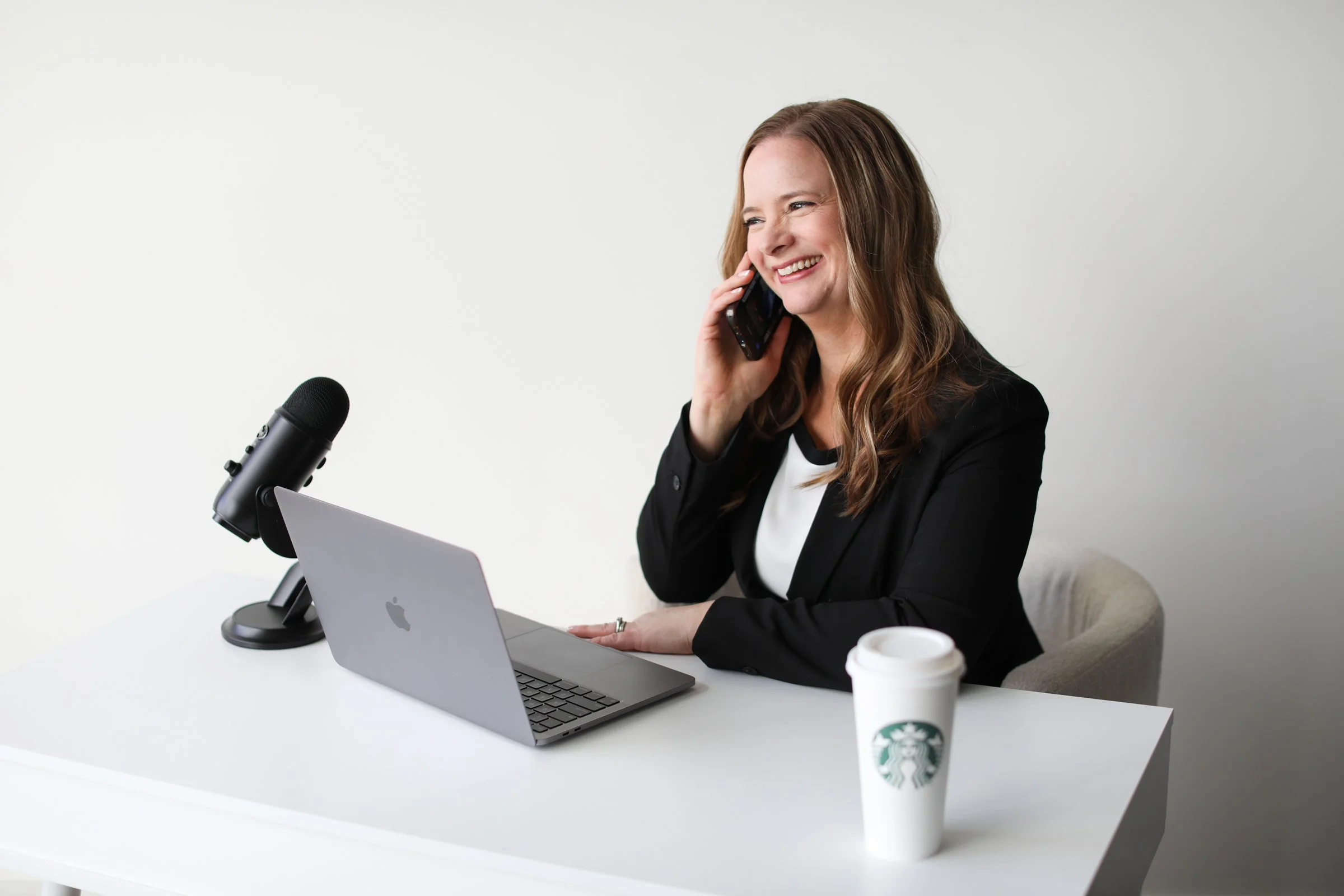 Female business owner working at a desk, on the phone laughing, with Mac Book  open