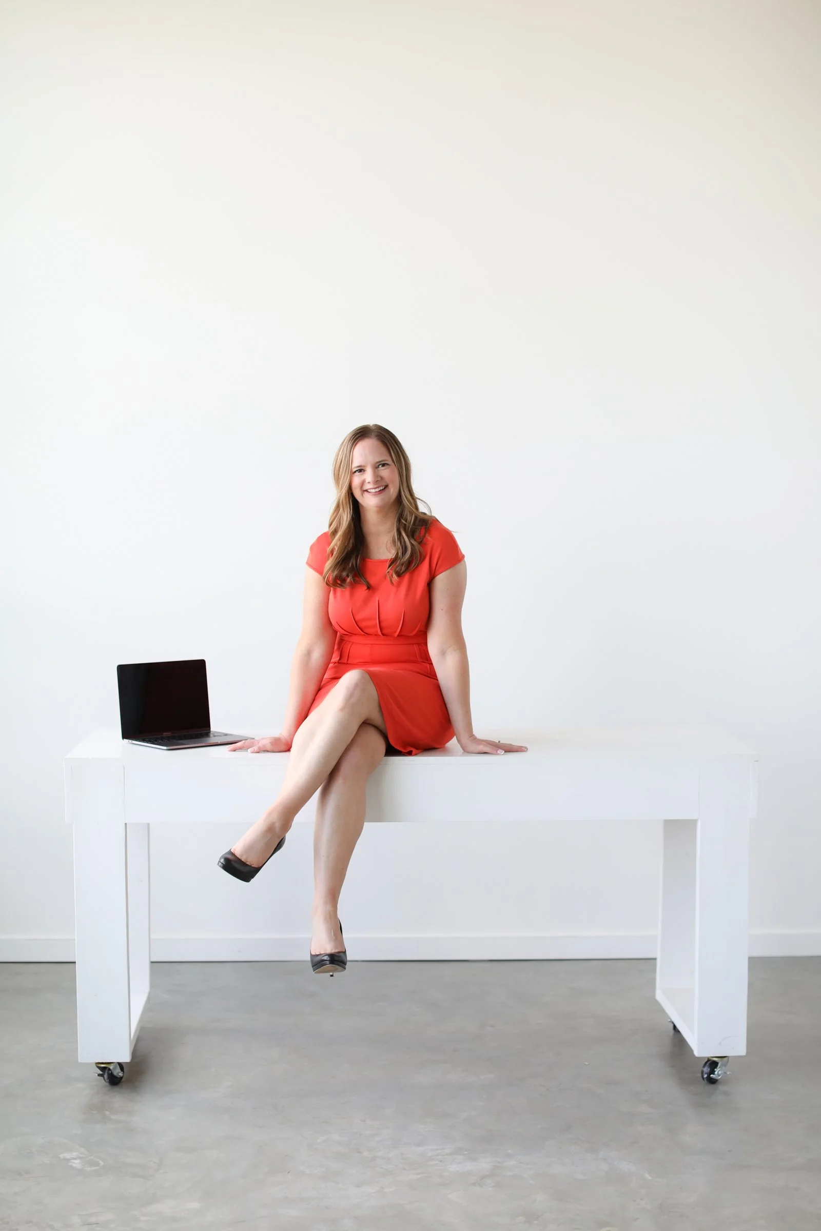 Grit Fueled Owner and CEO sitting on a desk next to a laptop, smiling at you