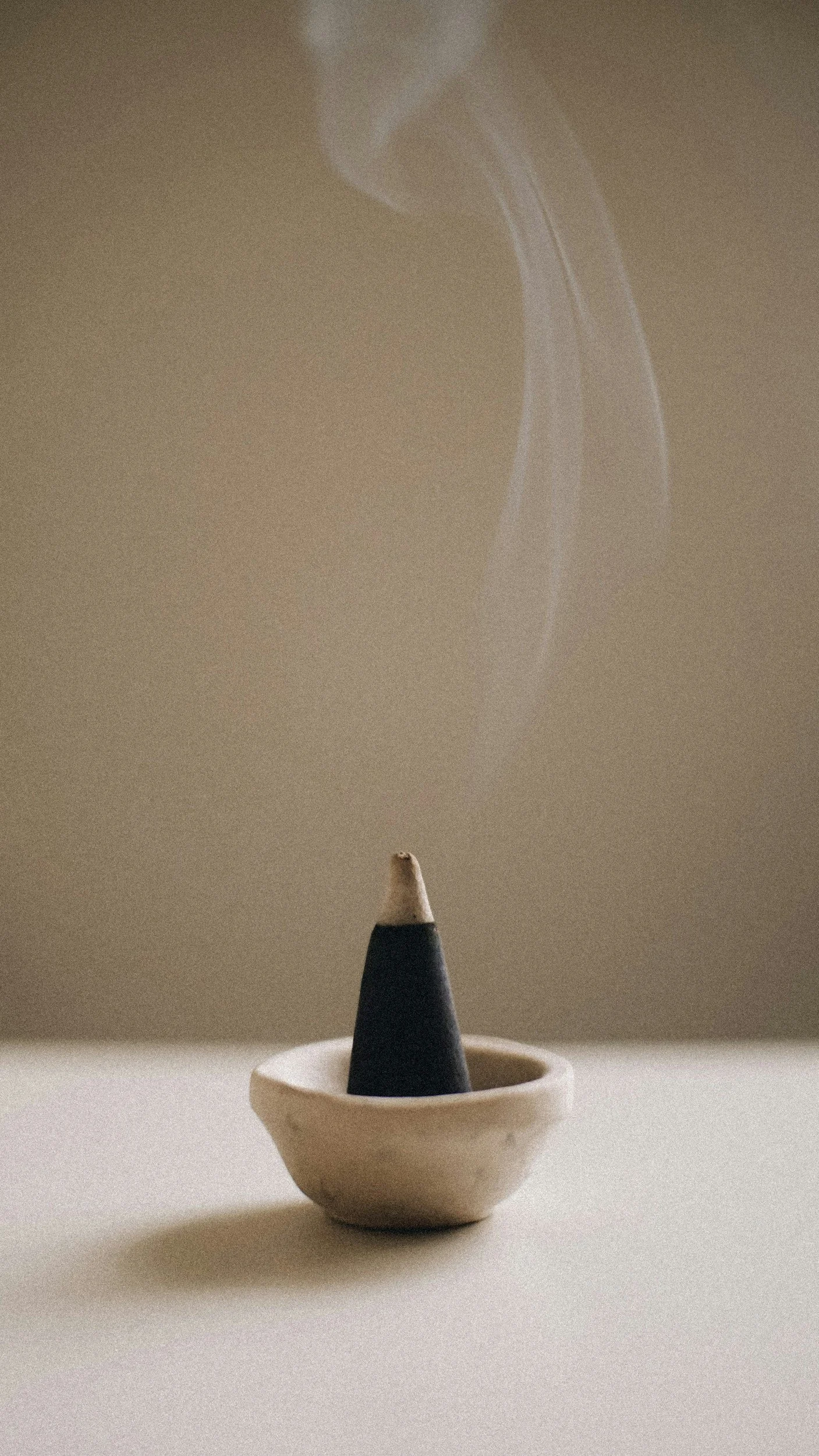 A cone-shaped incense holder with smoke curling upward against a beige background.