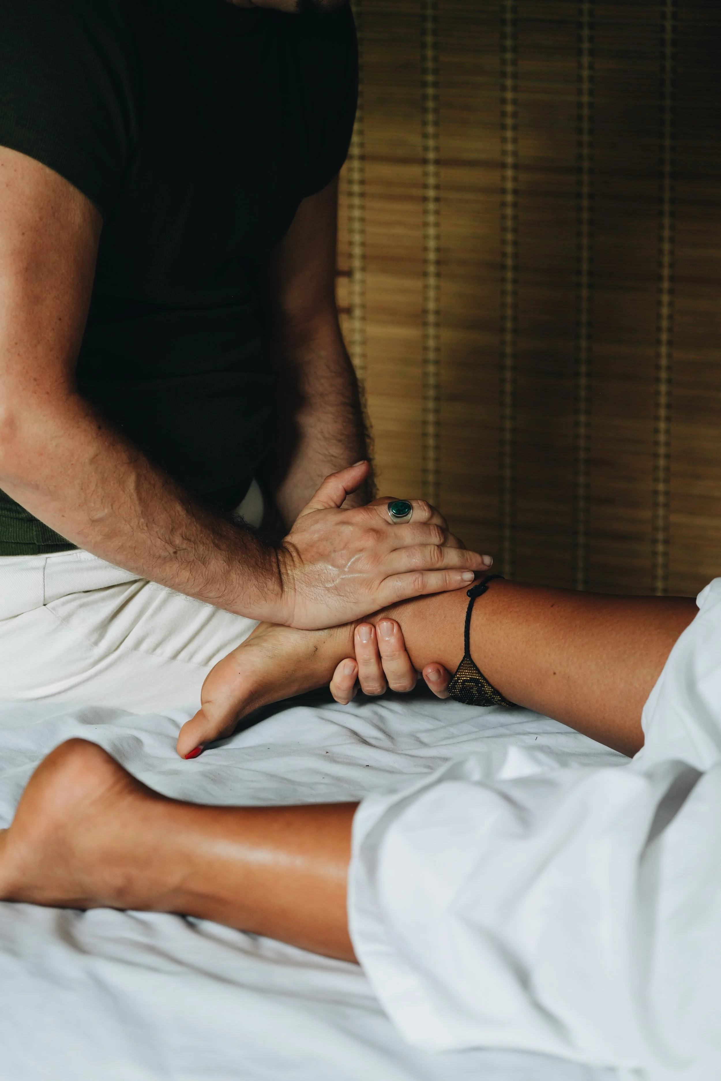 Person receiving a massage or physical therapy on their leg from a practitioner, in a room with wooden blinds in the background.