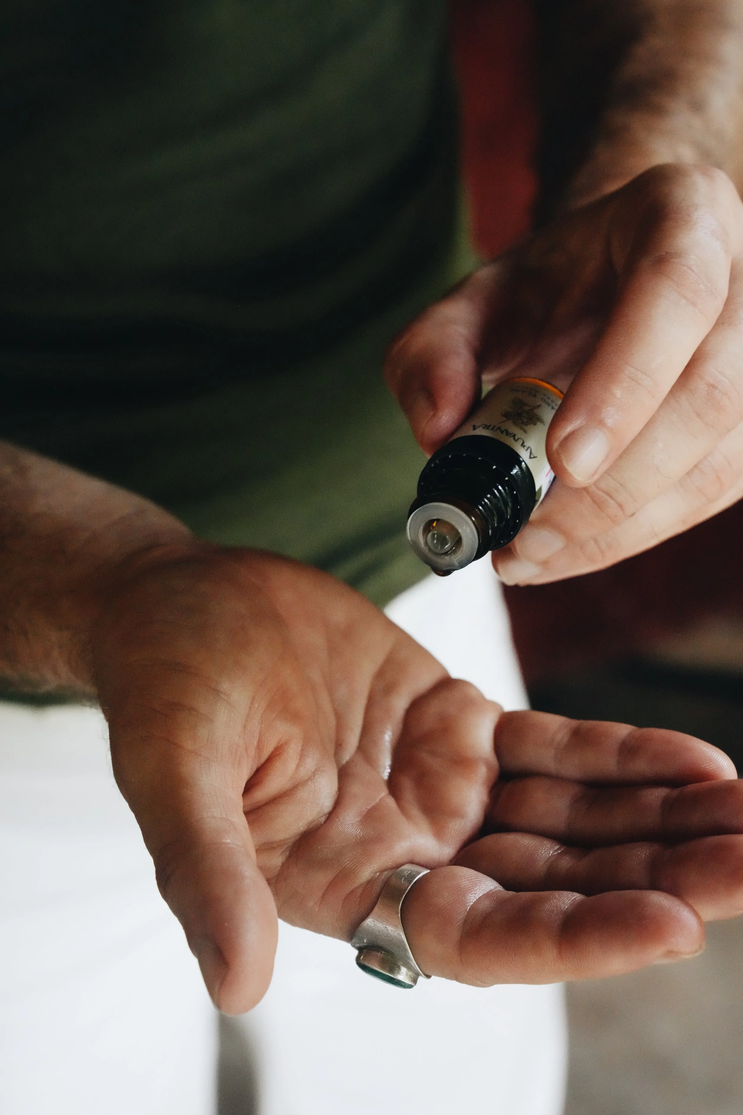 A person dispensing essential oil onto their open palm from a small dark brown bottle.