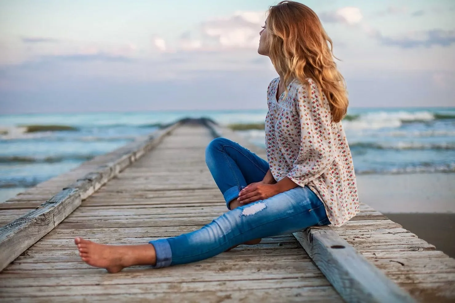 Sad woman sitting alone on a dock looking out at the ocean on a cloudy day