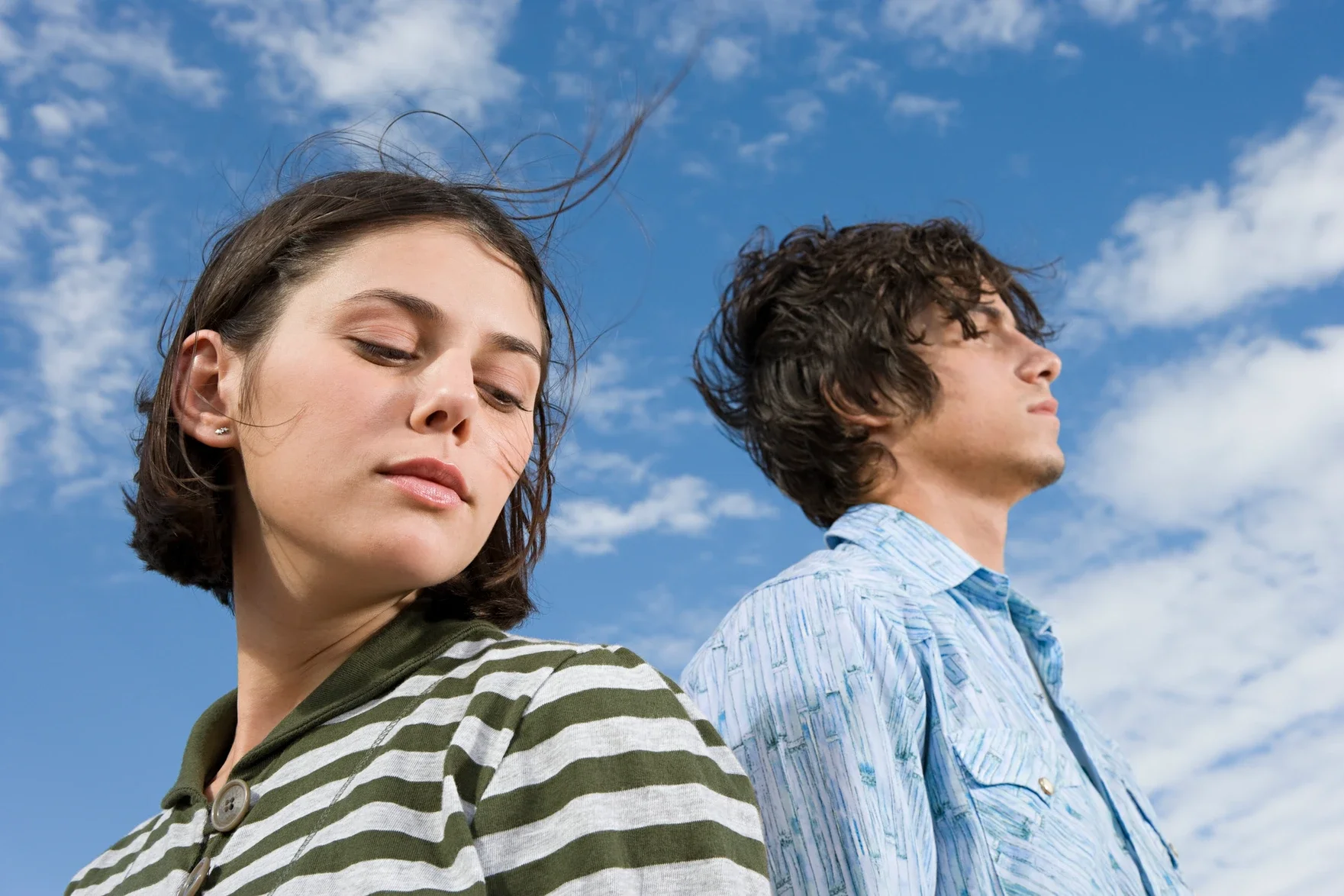 One female and one male young adult outside under a blue sky looking away from each other