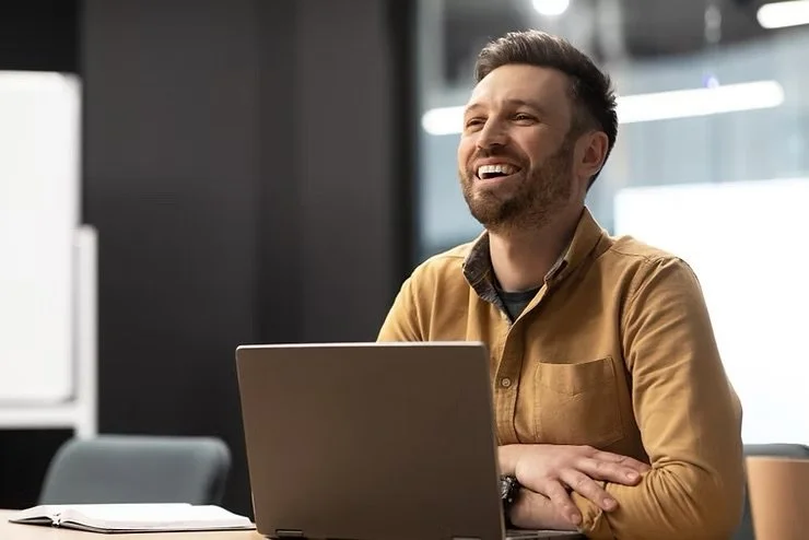 Smiling man sitting at a desk with his computer, demonstrating good mental health