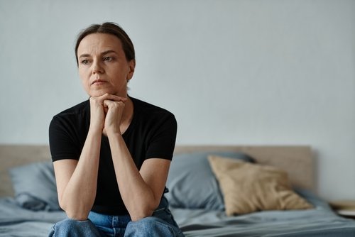 Middle aged caucasian woman sitting on a bed, looking sad