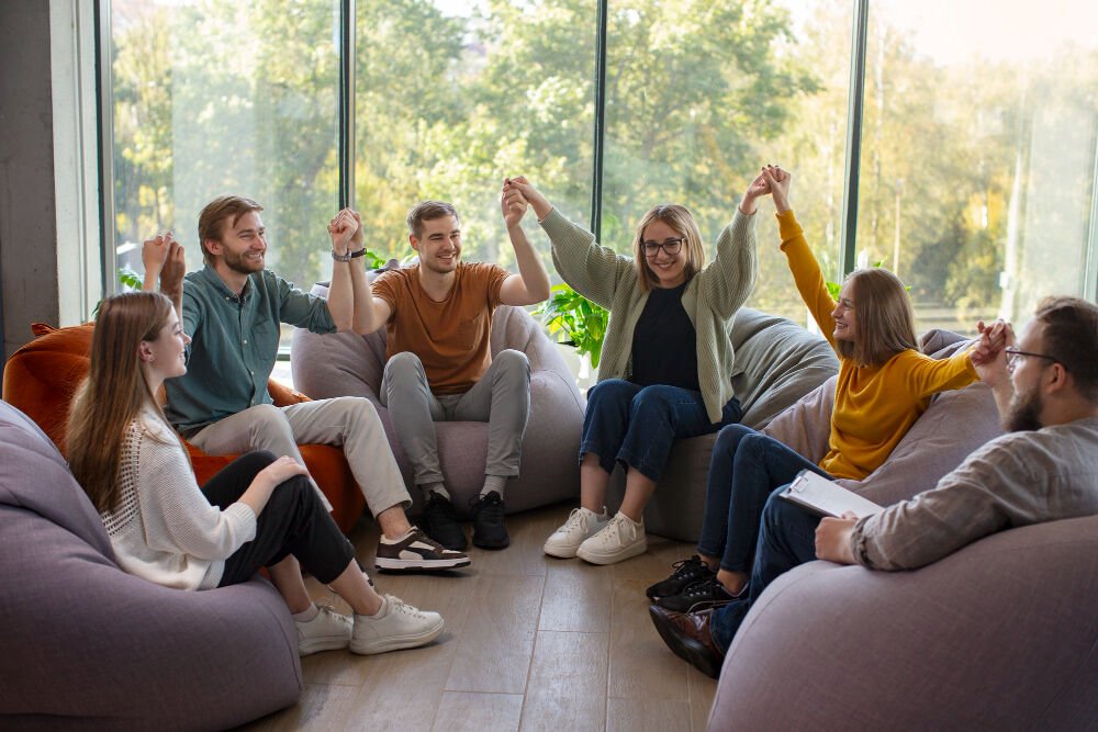 Several individuals sitting in a circle for group therapy holding hands and smiling