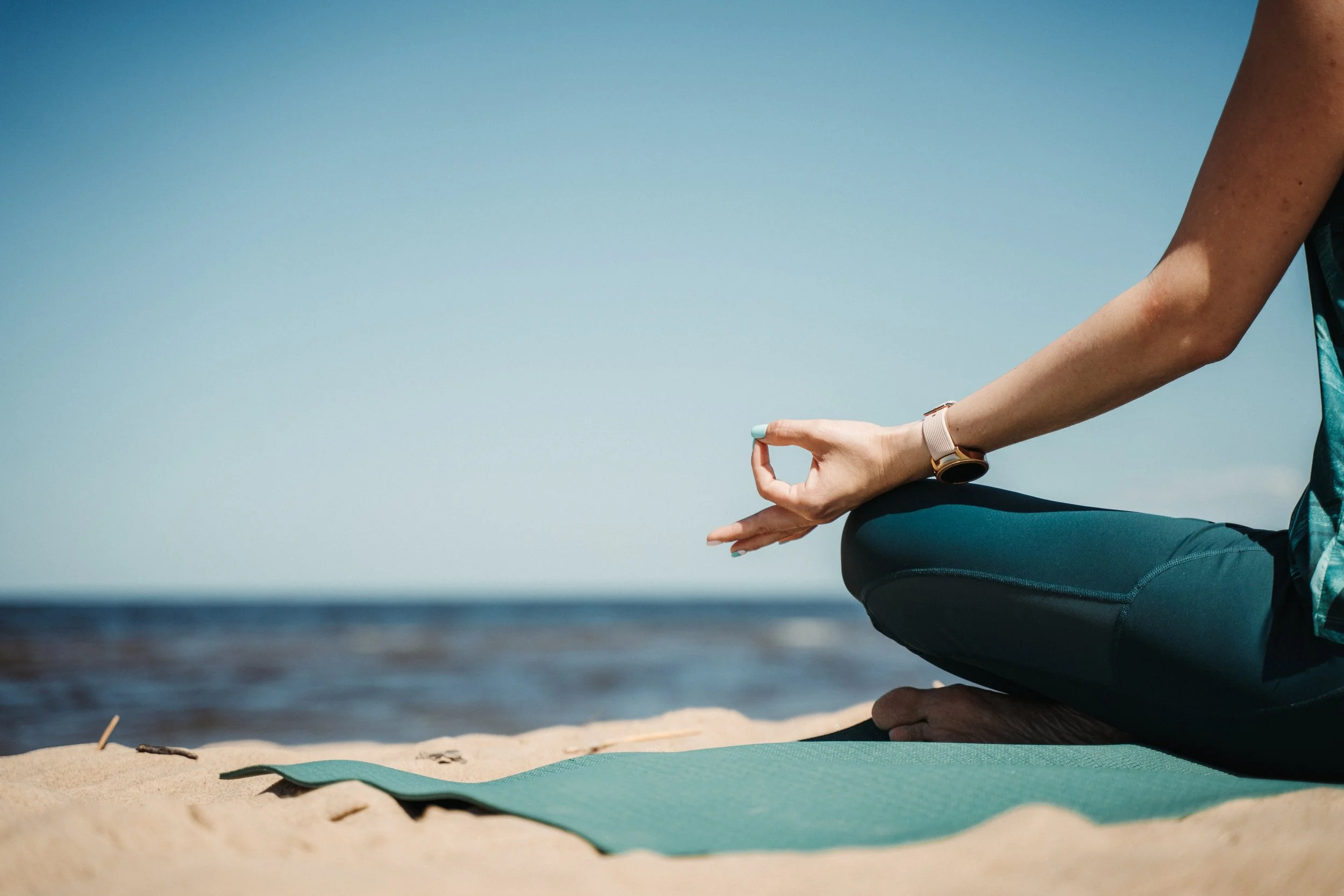 Woman sitting on the beach in a yoga pose with the ocean in front of her