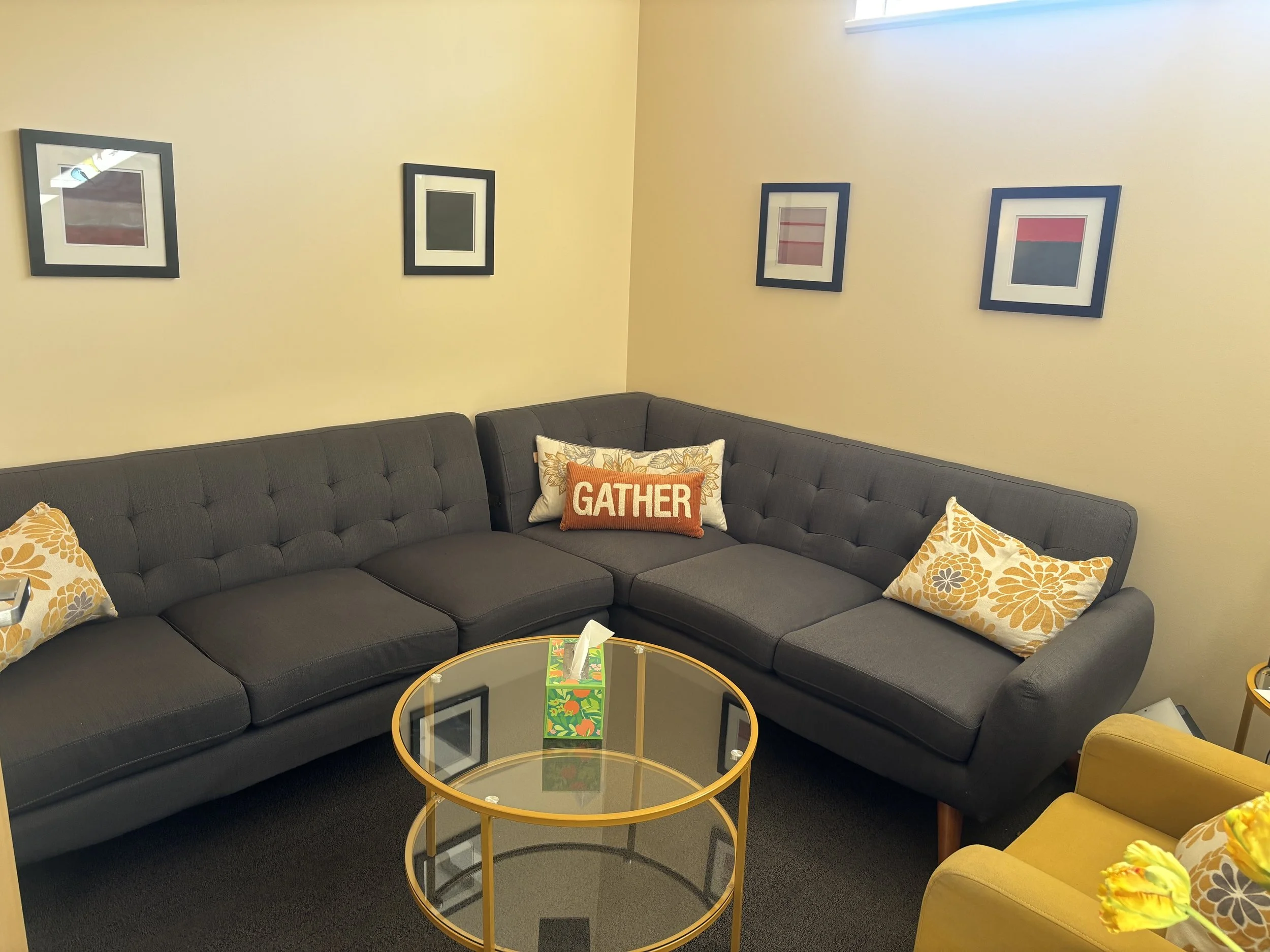 Therapist office  with yellow walls, a comfy gray couch with throw pillows.