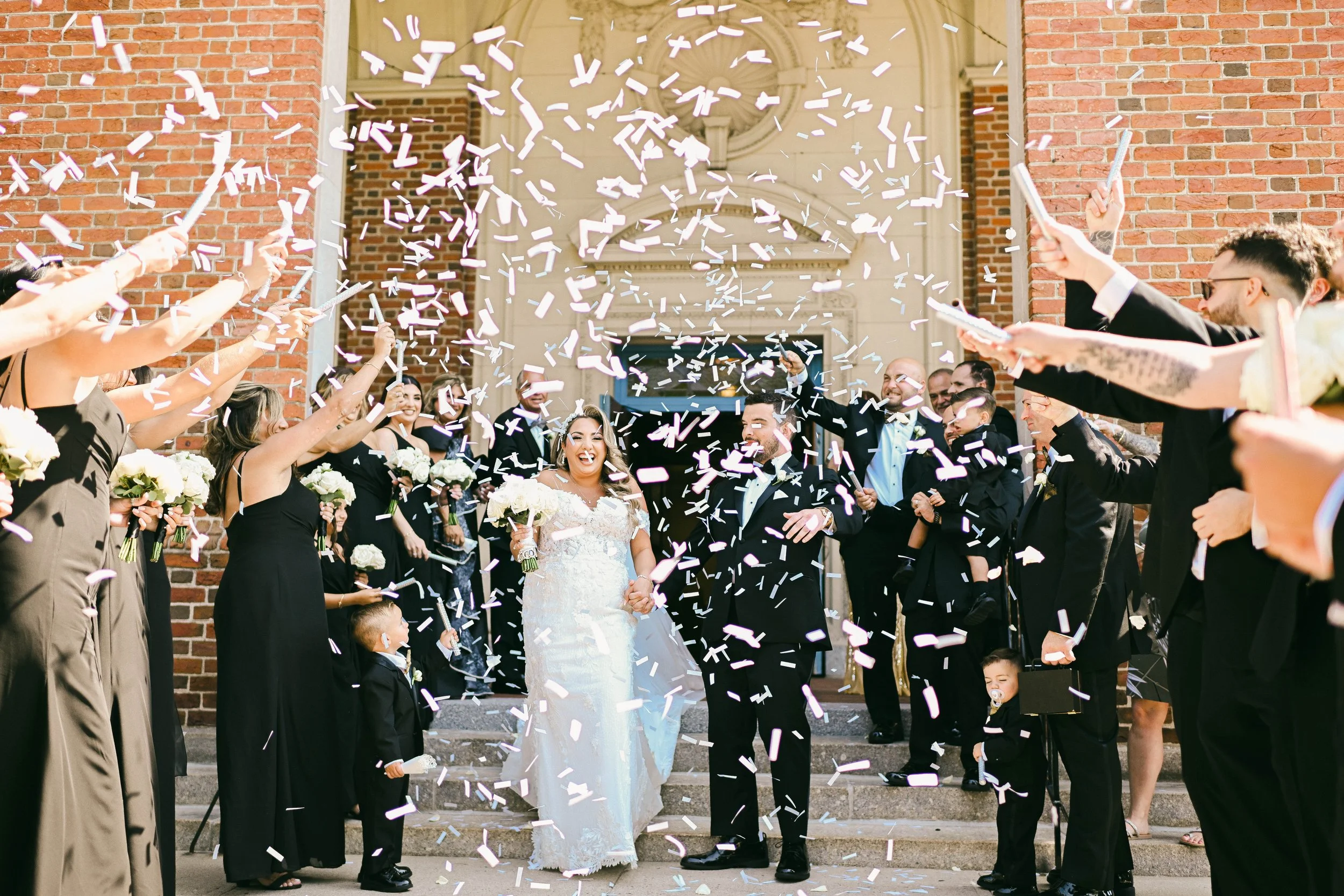 A wedding celebration with the bride and groom exiting a building as guests throw confetti in the air.