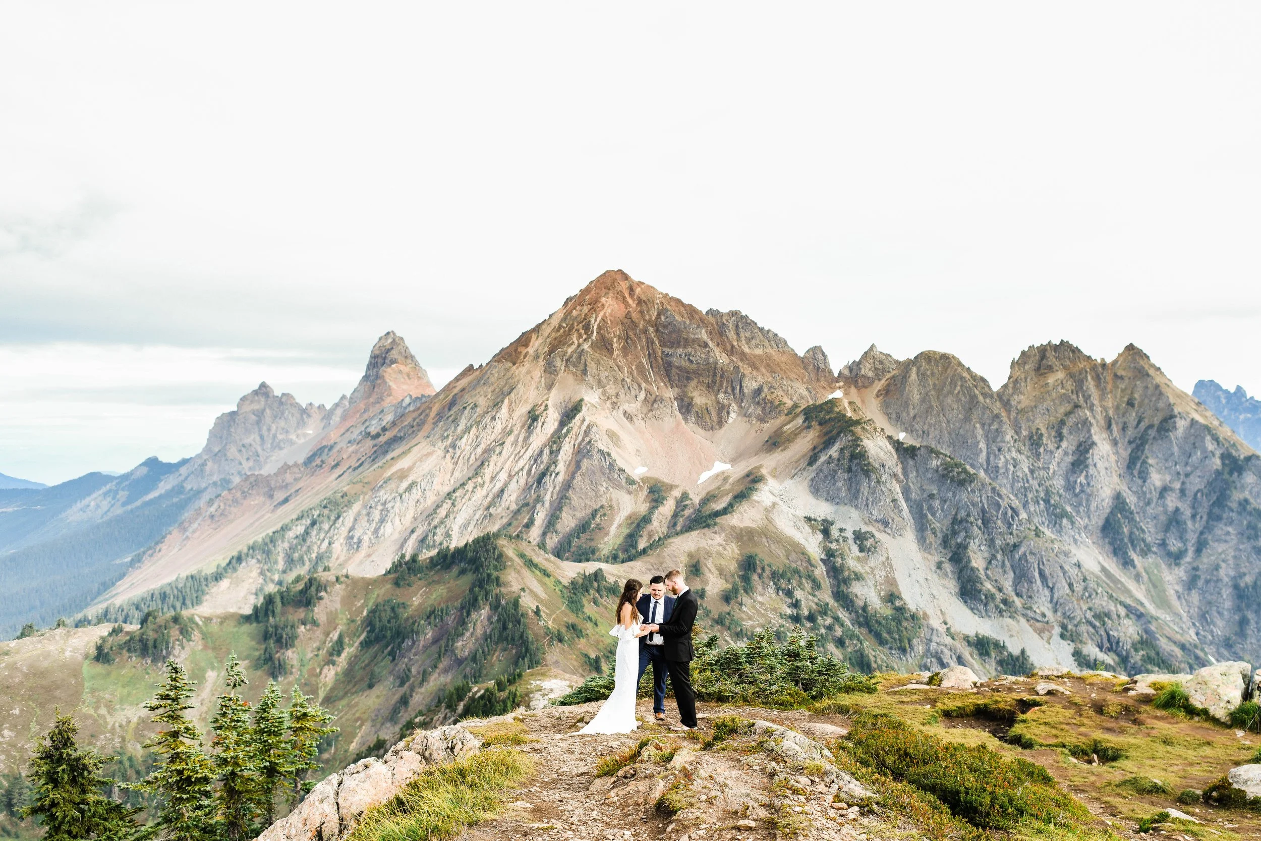 A wedding ceremony taking place on a rocky ledge in front of a mountain range with rugged peaks.