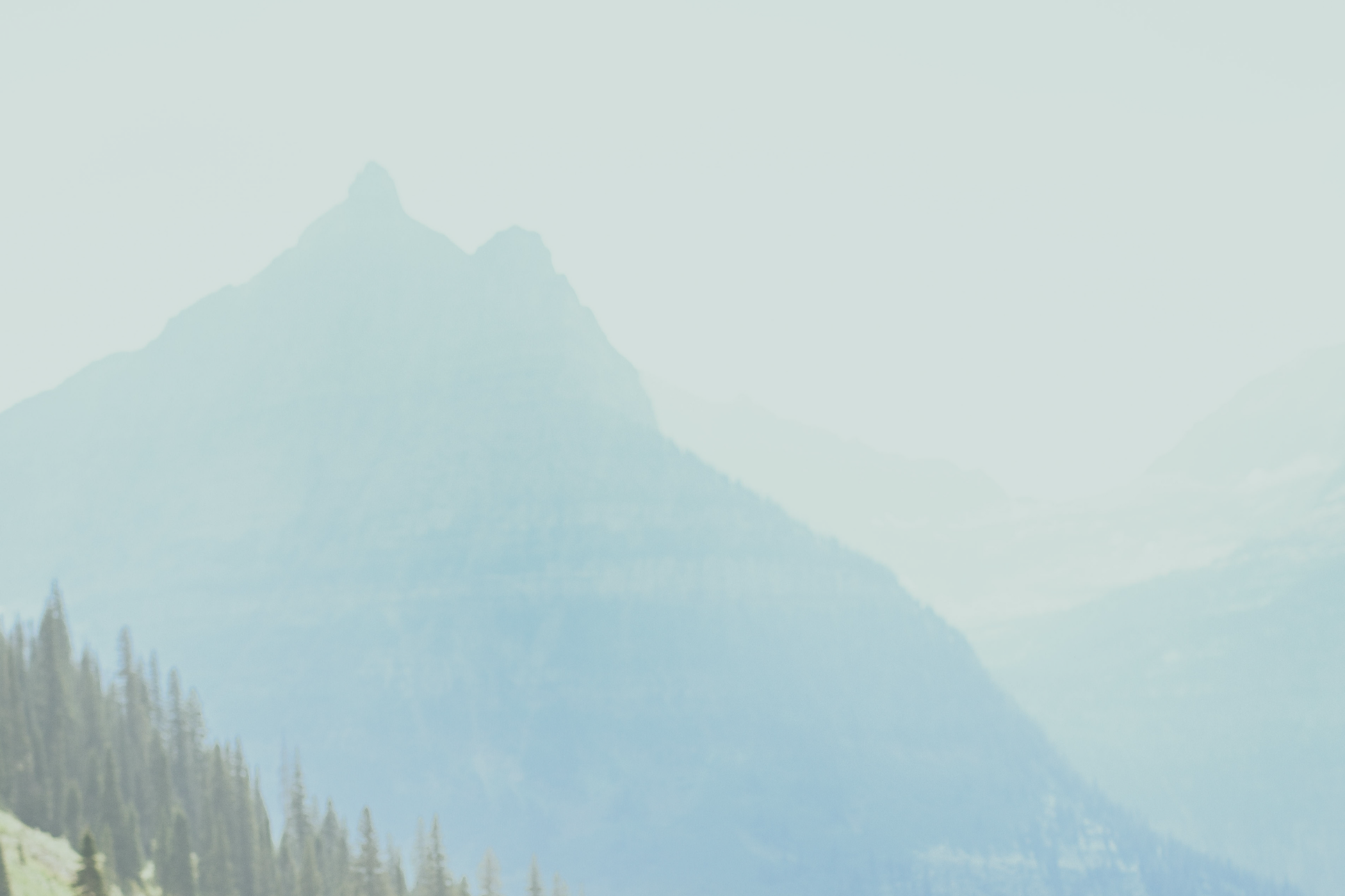 A mountain landscape with a prominent peak, surrounded by forested slopes and hazy sky.