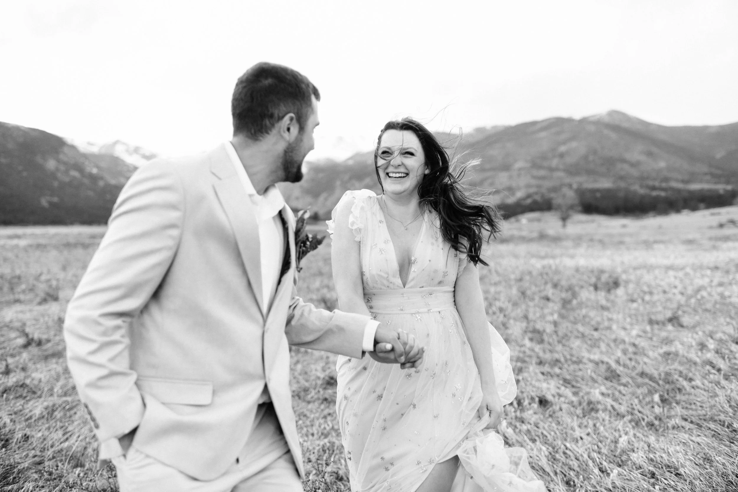 A happy couple holding hands and laughing outdoors with mountains in the background.