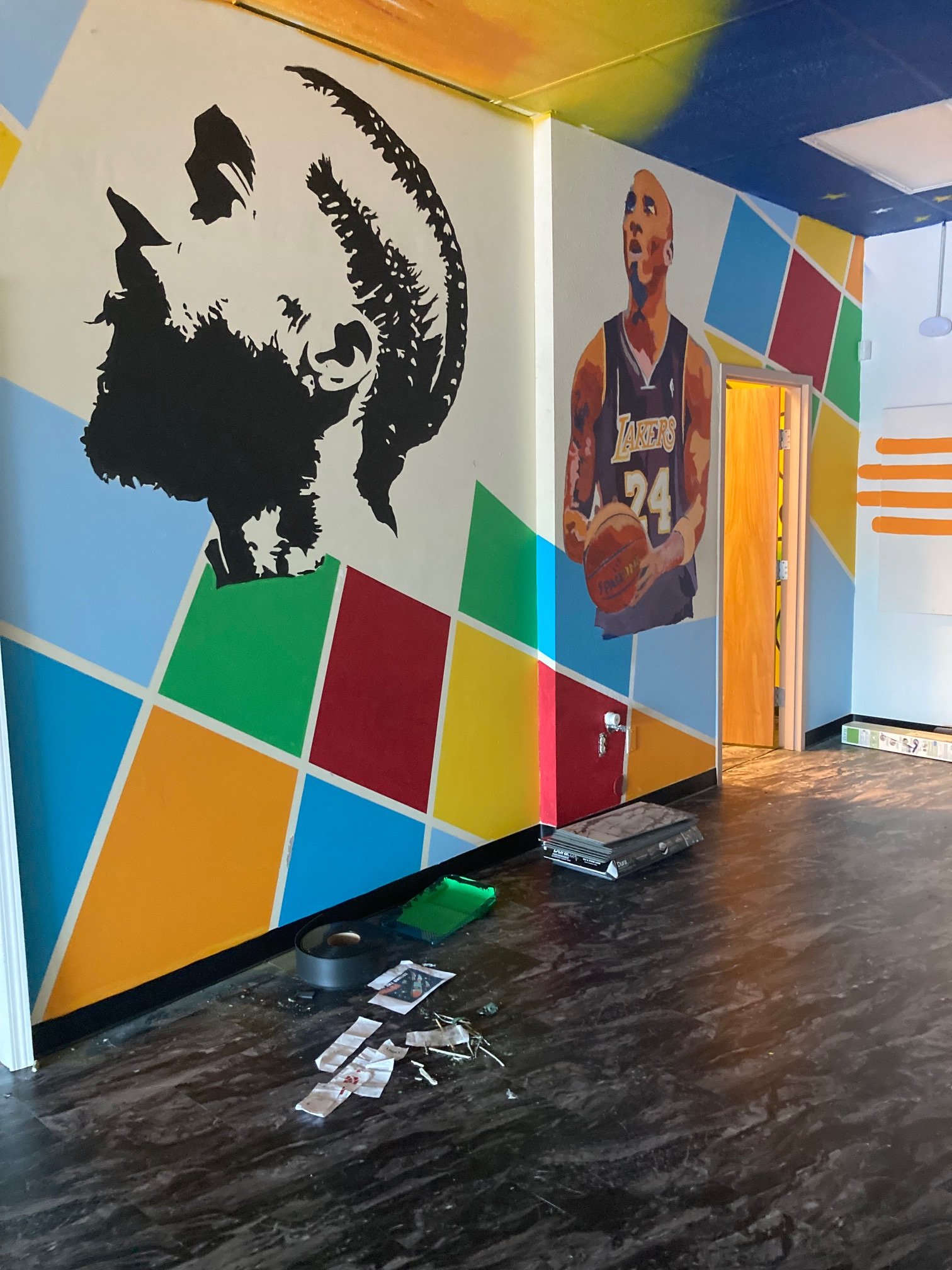 Colorful mural featuring a black and white portrait of a man with a beard and a painting of basketball player Kobe Bryant holding a basketball, with geometric colored shapes in the background.
