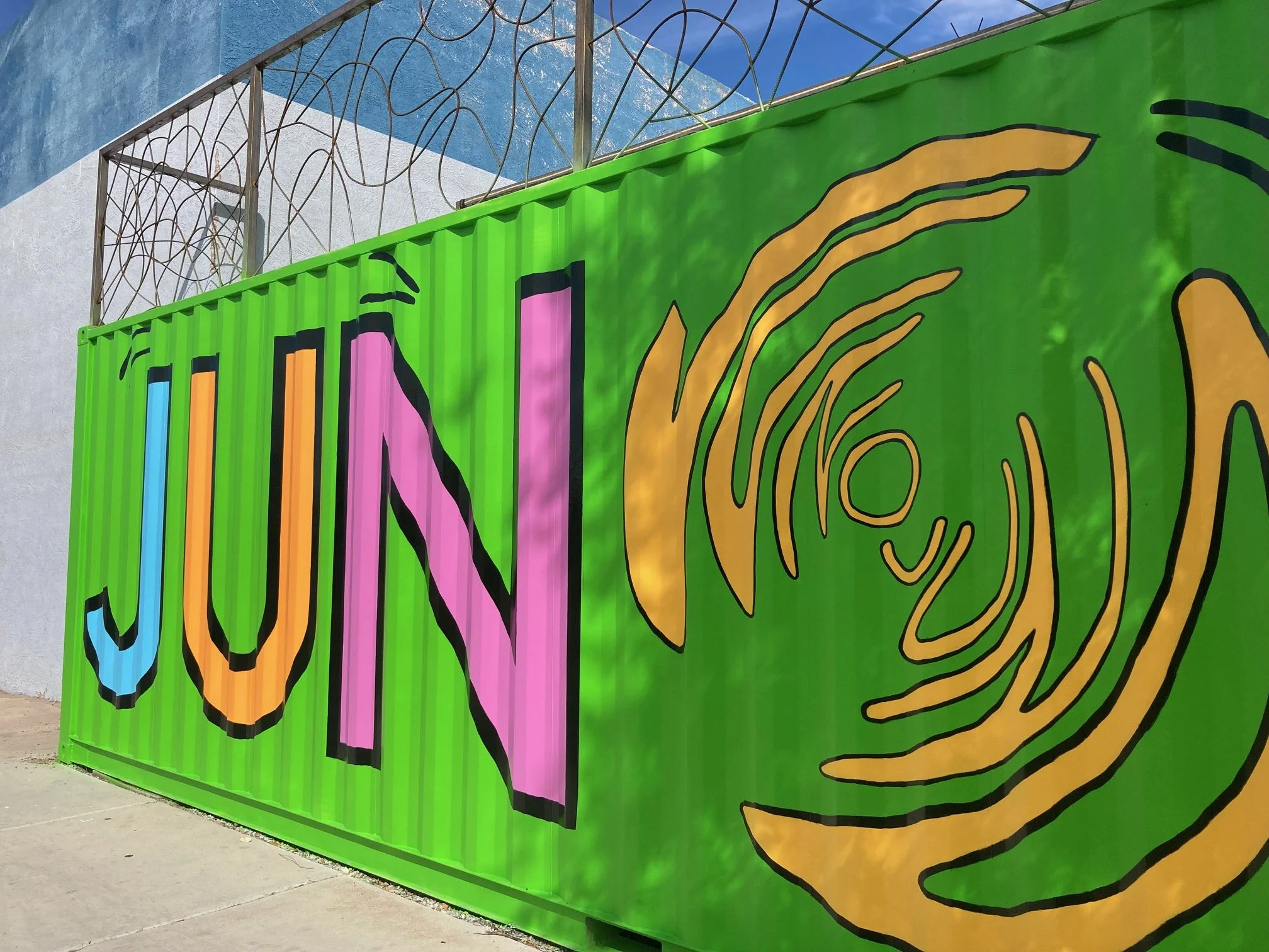 Colorful mural on a green wall with the word 'JUN' in large pastel letters and abstract yellow lines.