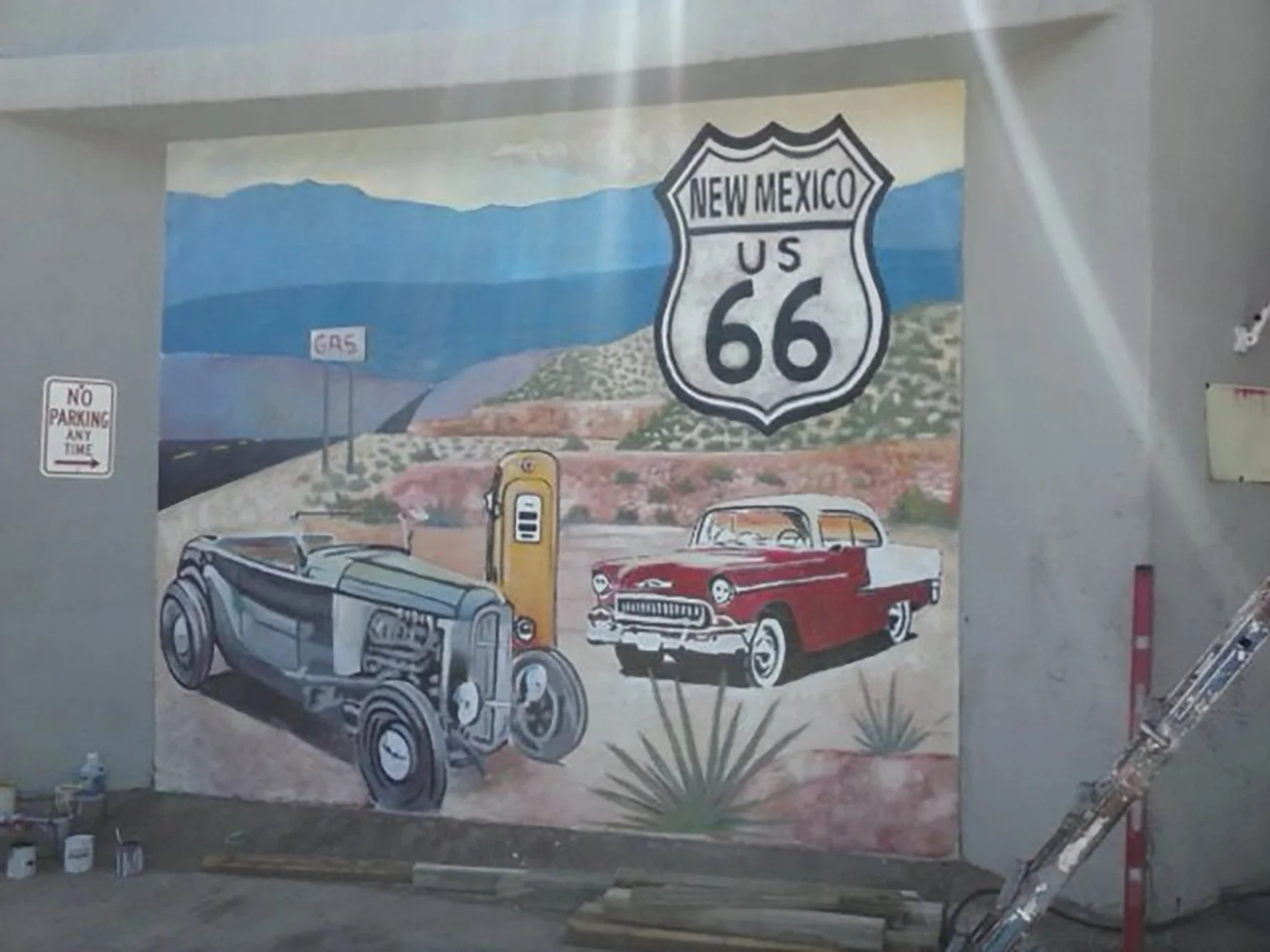 Mural depicting Route 66 scenes in New Mexico, with vintage cars, a gas pump, and mountains.