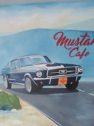 Painting of a vintage black and white car driving on a road with a blue sky background, and a sign reading 'Mustang Cafe'