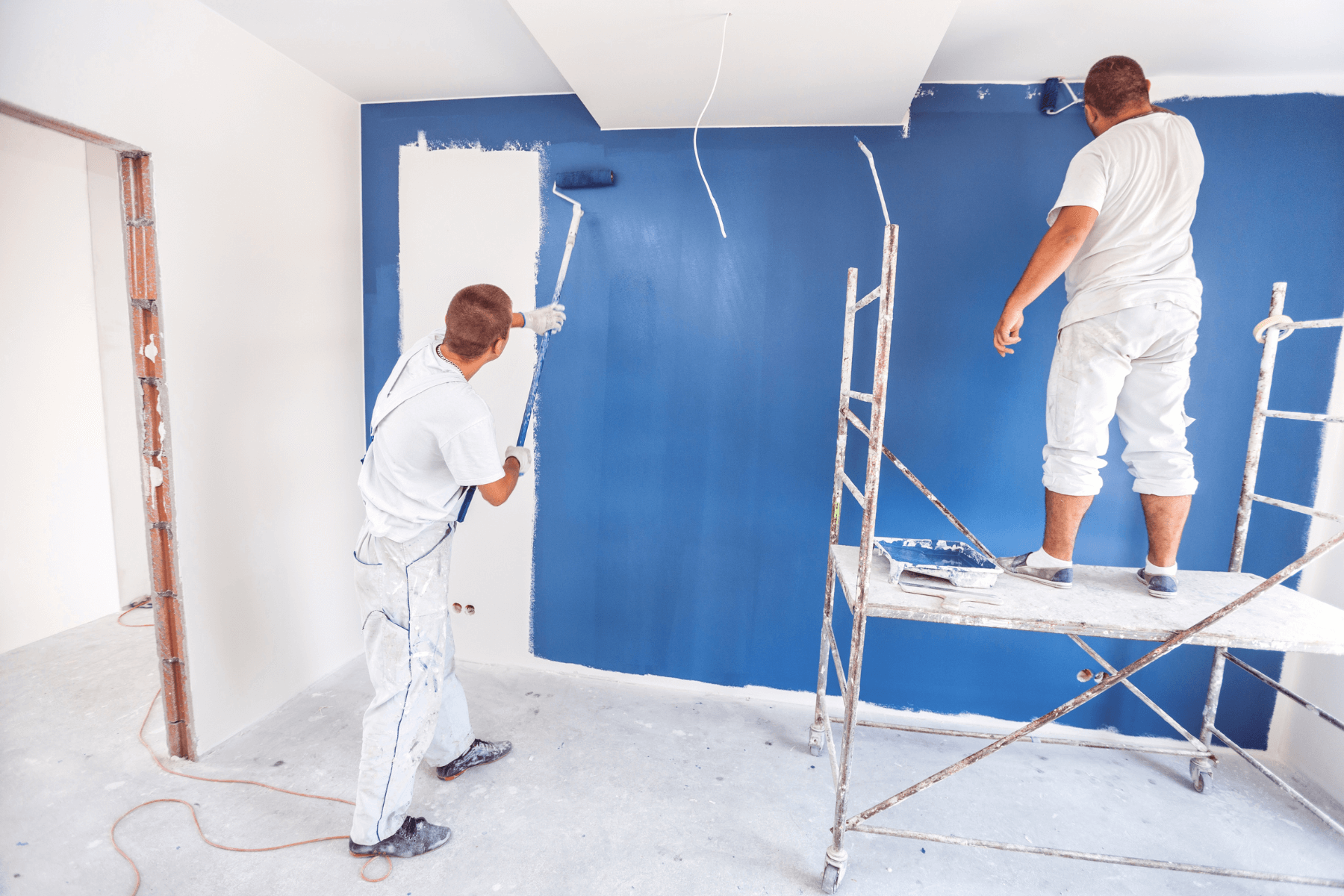 Two guys using scaffolding and rollers to paint an interior wall blue