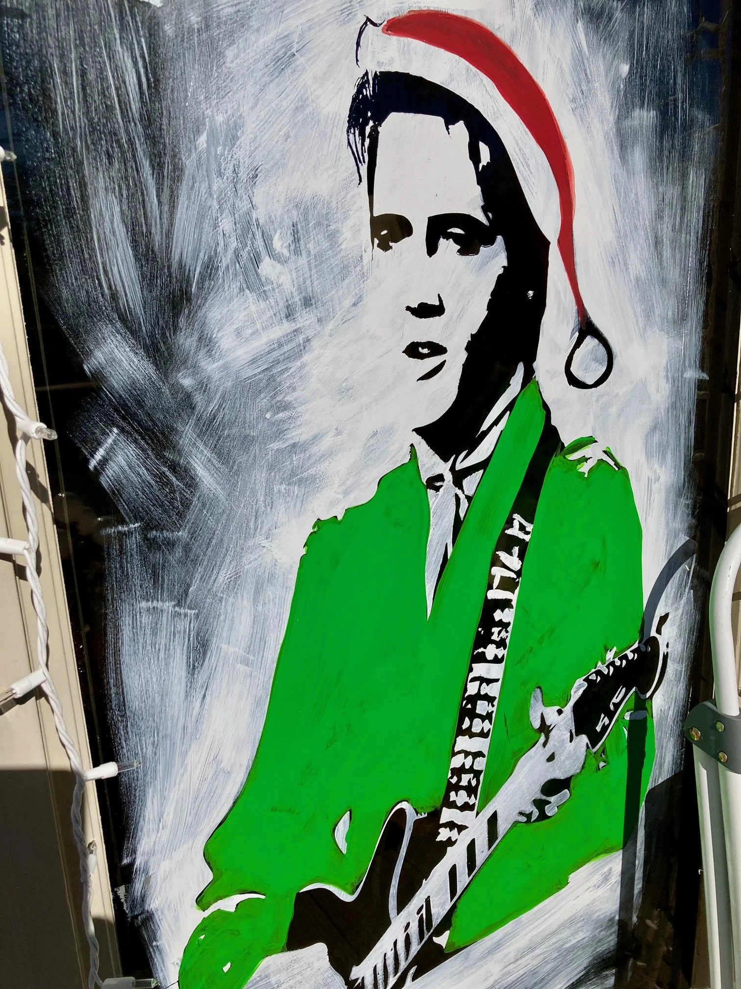 A stylized painting of a woman with black hair, wearing a red Santa hat and green jacket, holding a guitar against a background with white and gray brush strokes.