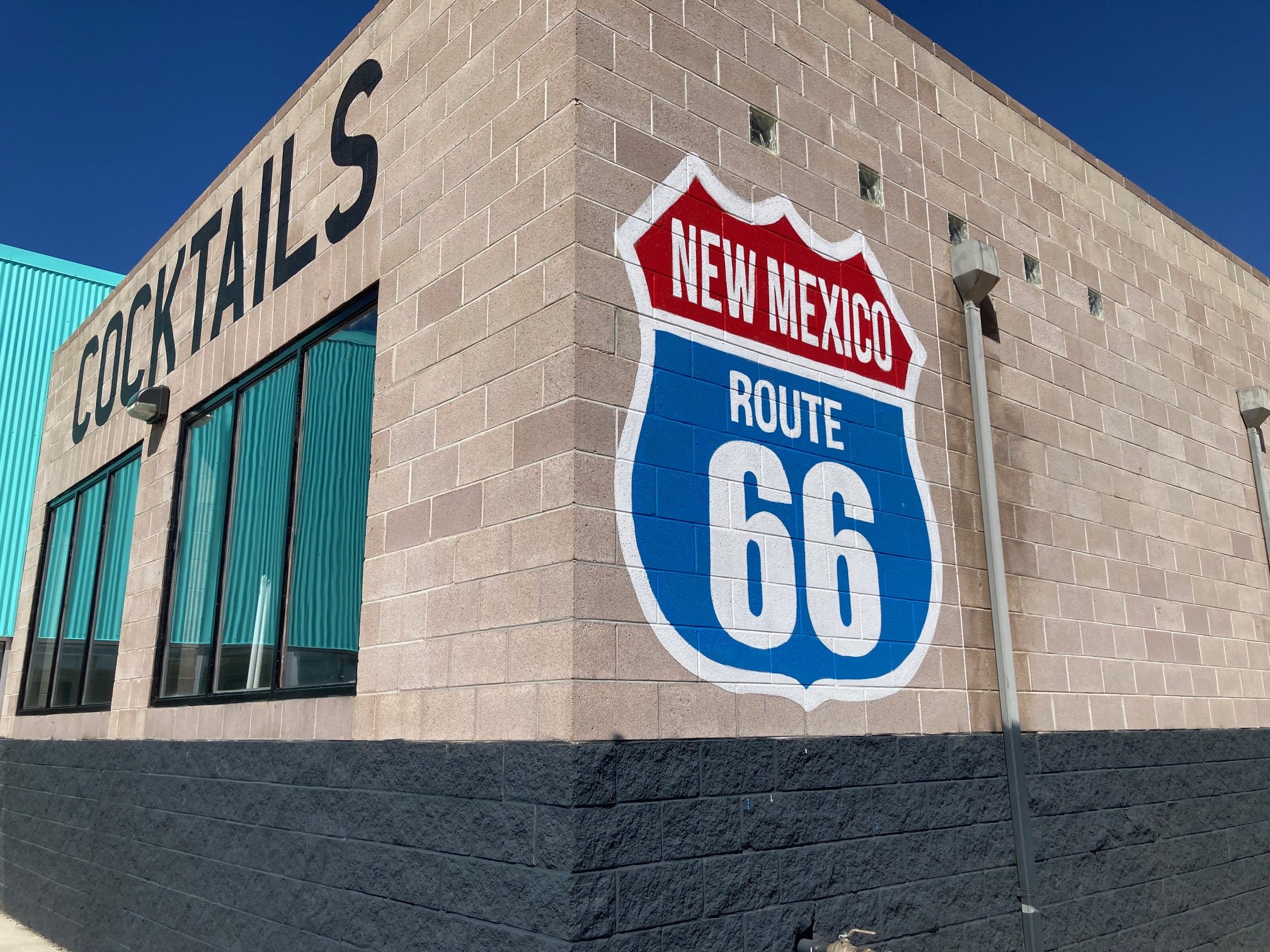 A painted sign on a building depicting the Route 66 shield with 'New Mexico' written on a red background banner at the top and 'Route 66' in the center on a blue background.  Custom mural artist Billings, Montana.